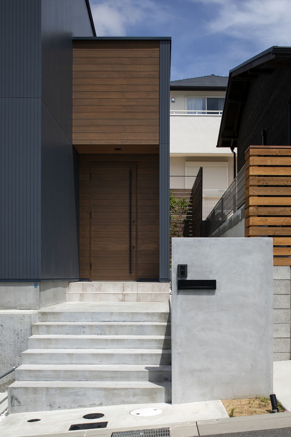 コンクリートの階段を上がった先にある木製の扉の玄関・デザイン住宅 注文住宅・デザイン住宅建築実例_『CASE629 Con』_外観