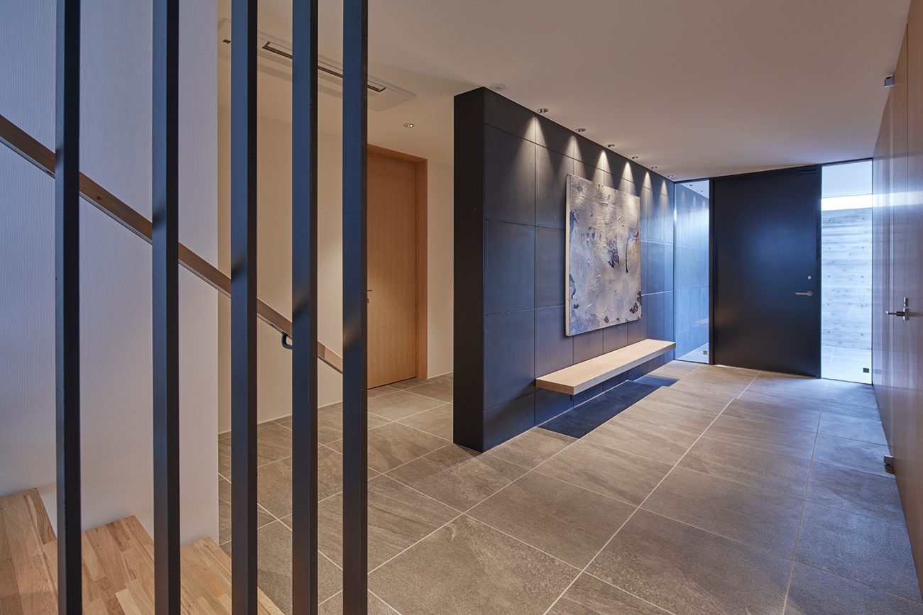 グレーのタイル床で、木製のベンチが取り付けられた黒い壁がある玄関・デザイン住宅 注文住宅・デザイン住宅建築実例_『CASE632 H邸（社長の邸宅）』_玄関