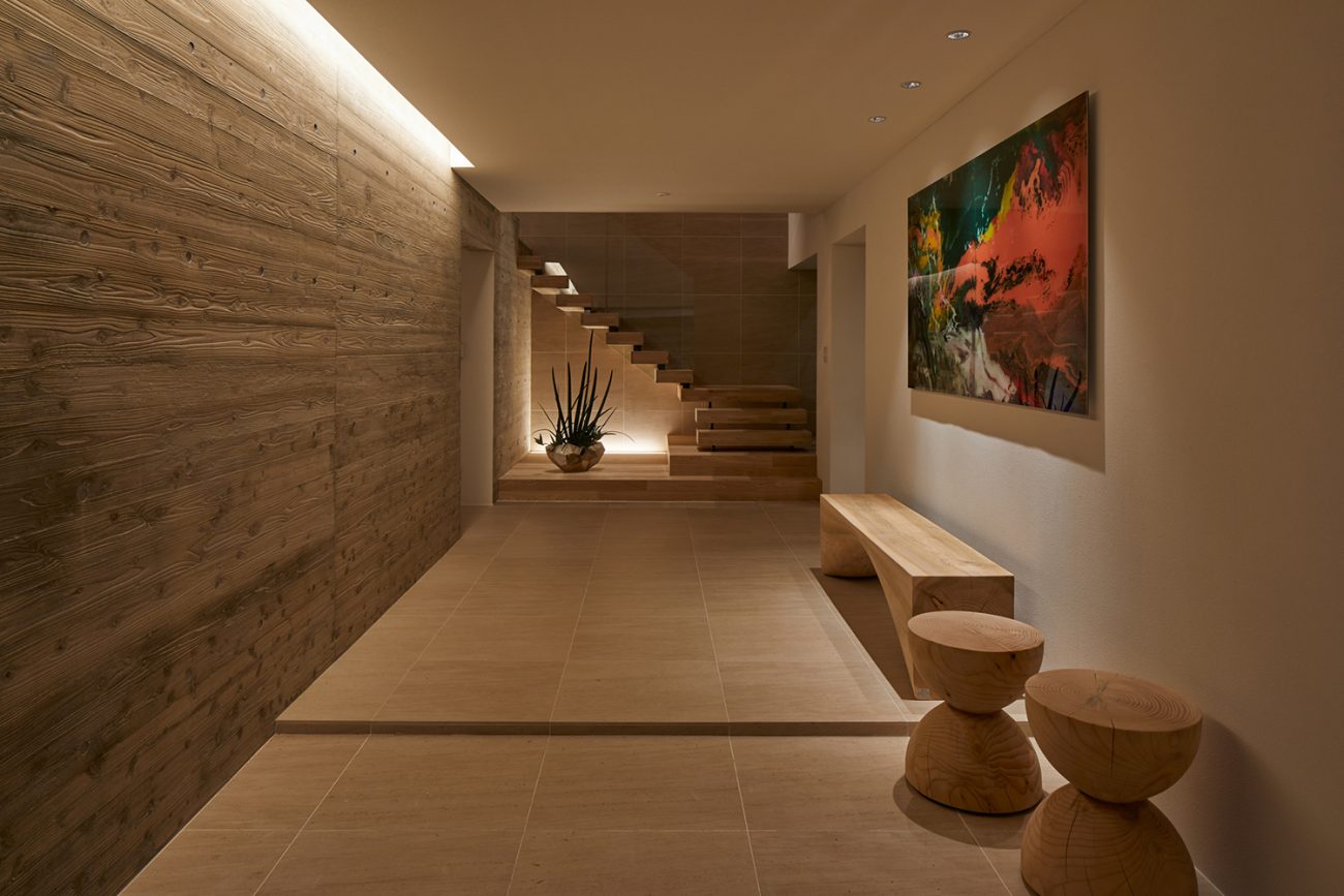正面に木製の階段があり、木のインテリアや絵画が飾られた空間・デザイン住宅 注文住宅・デザイン住宅建築実例_『CASE678 K邸（社長の邸宅）』_玄関