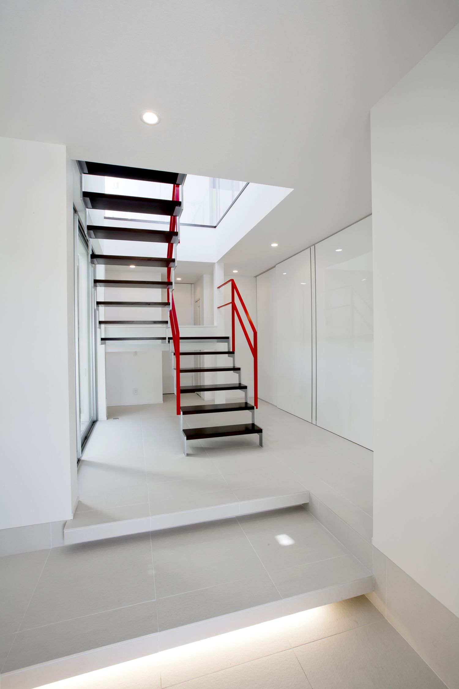 正面にスケルトン階段がある足元に間接照明を取り付けたスタイリッシュな白い玄関・デザイン住宅