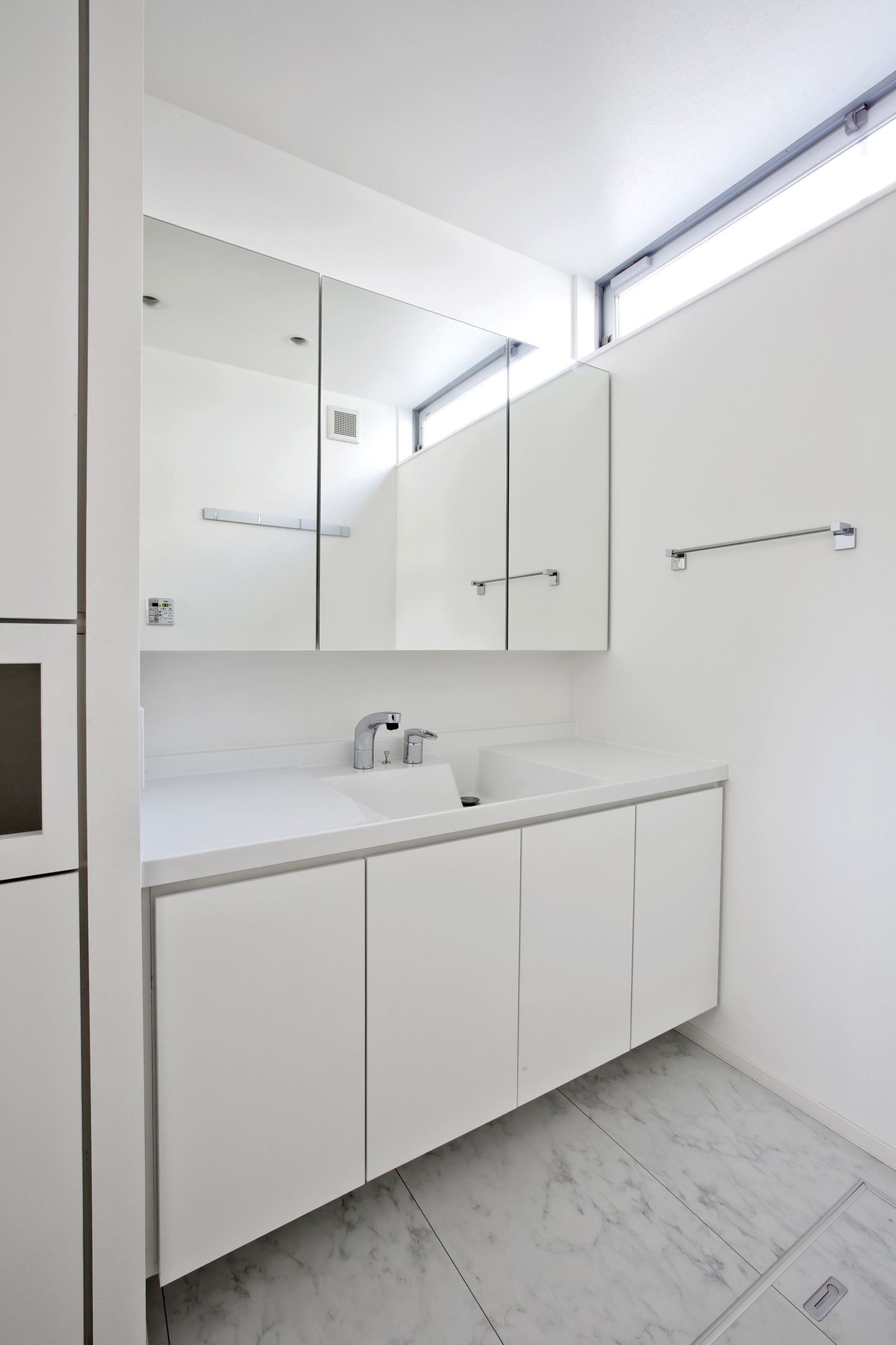 天井近くにスリット窓を取り付けたシンプルな白い洗面所・デザイン住宅