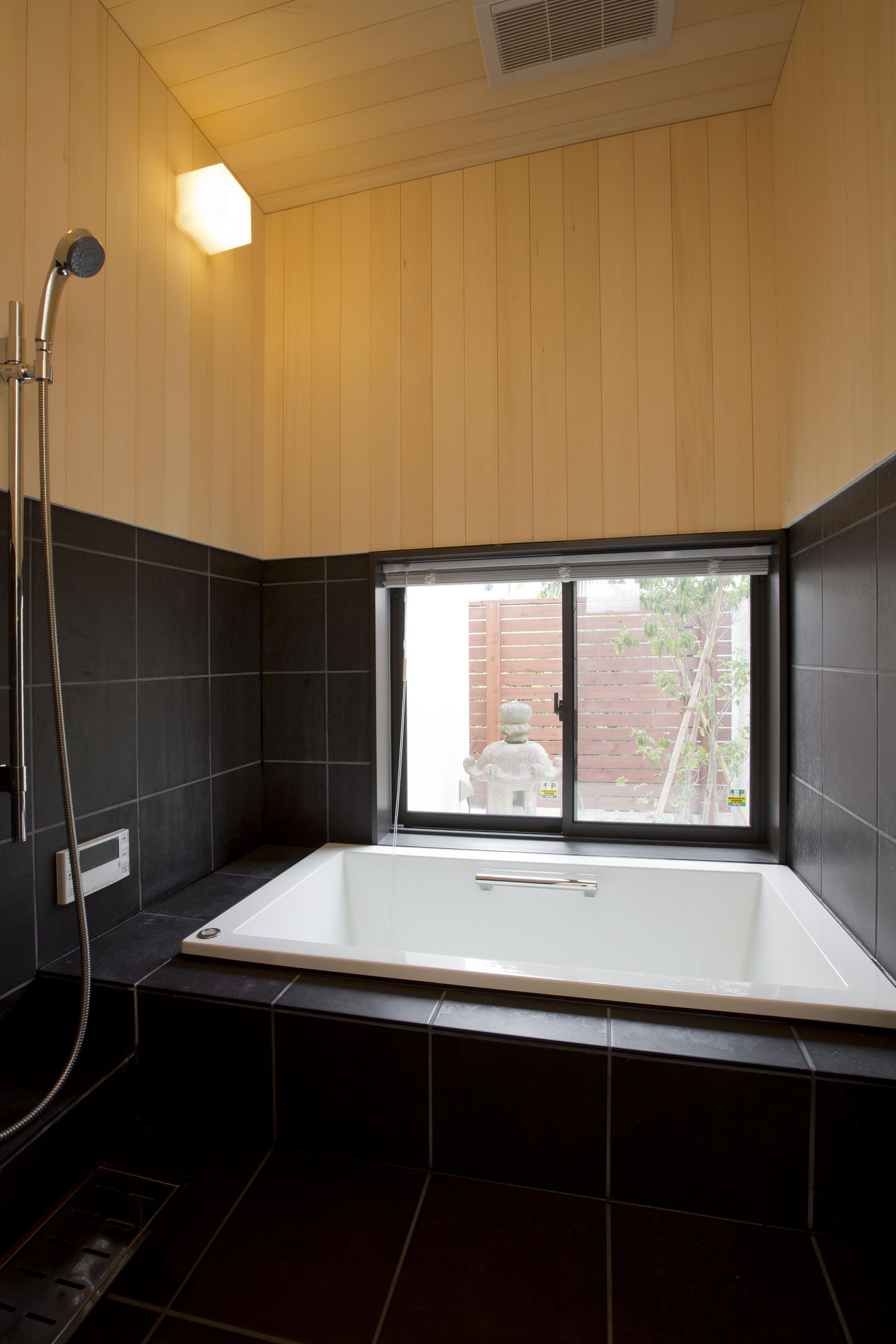 木目の壁とタイルの壁がある窓付きの和風な浴室・デザイン住宅