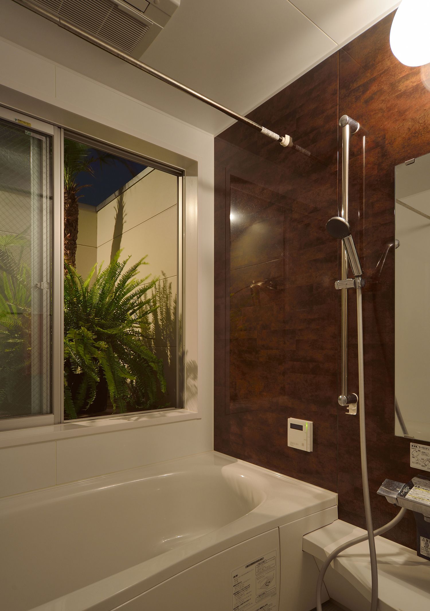 窓から緑が見える、木目のアクセントクロスが取り付けられた浴室・デザイン住宅