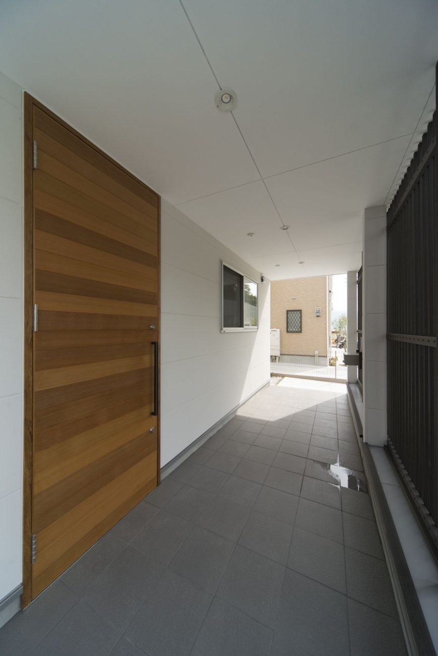 黒いルーバーの目隠しがある木の玄関扉の玄関ポーチ・デザイン住宅