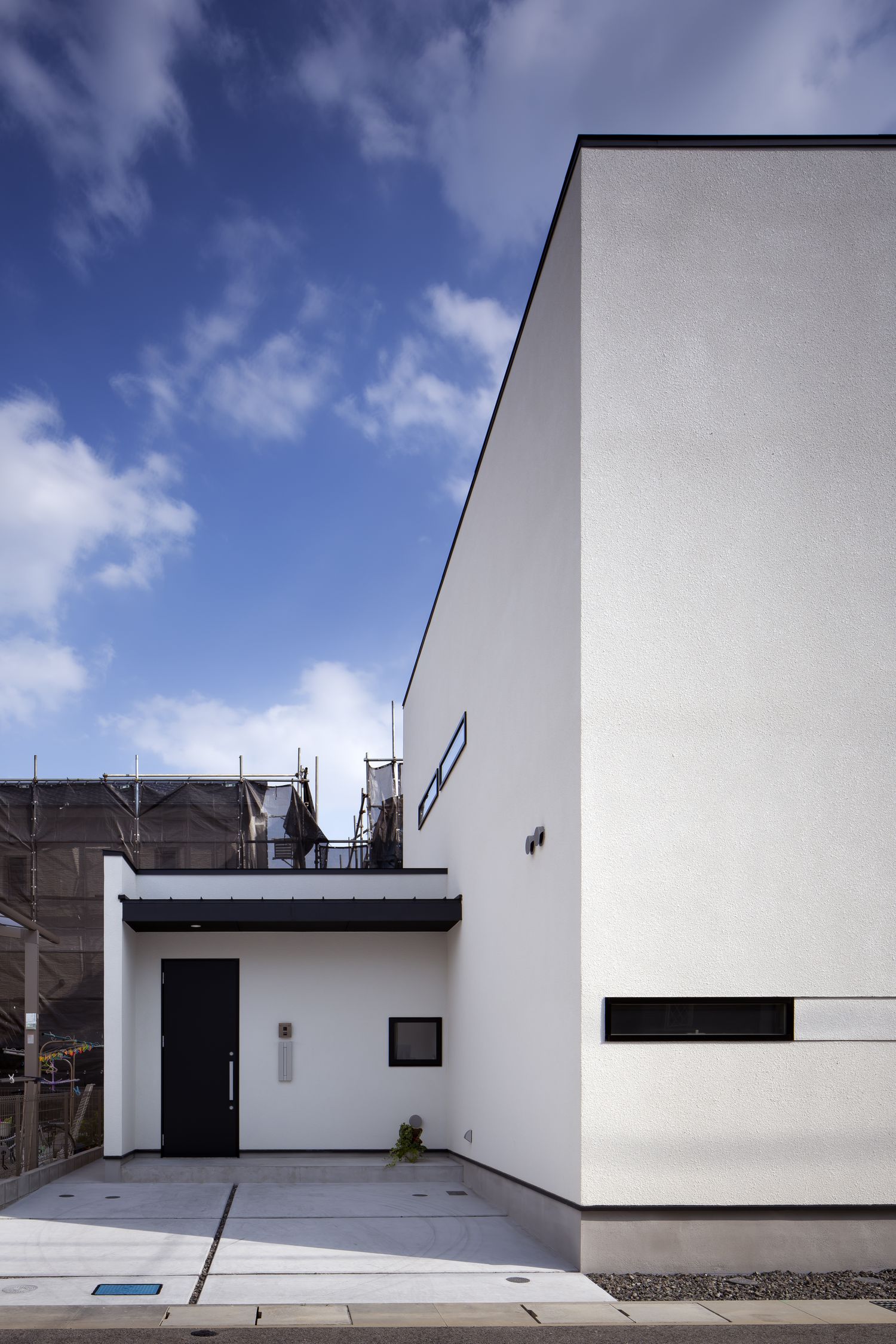 コンクリートのオープンな駐車スペースの奥にある玄関・デザイン住宅