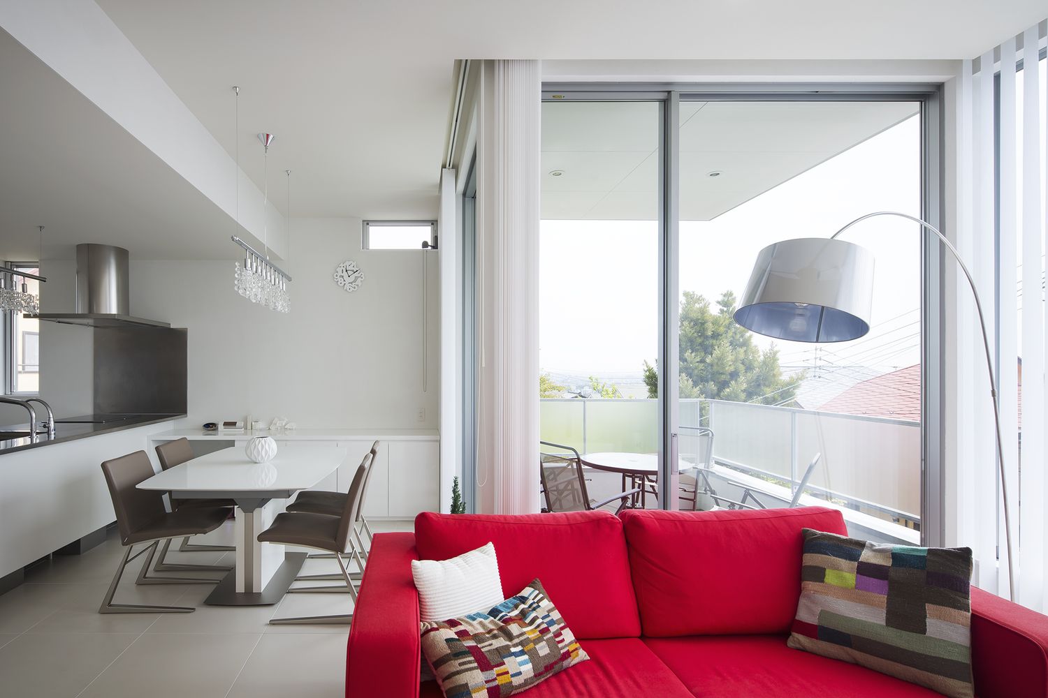 白い内装の中に赤いソファーがあるバルコニーに面した開放的なLDK・デザイン住宅