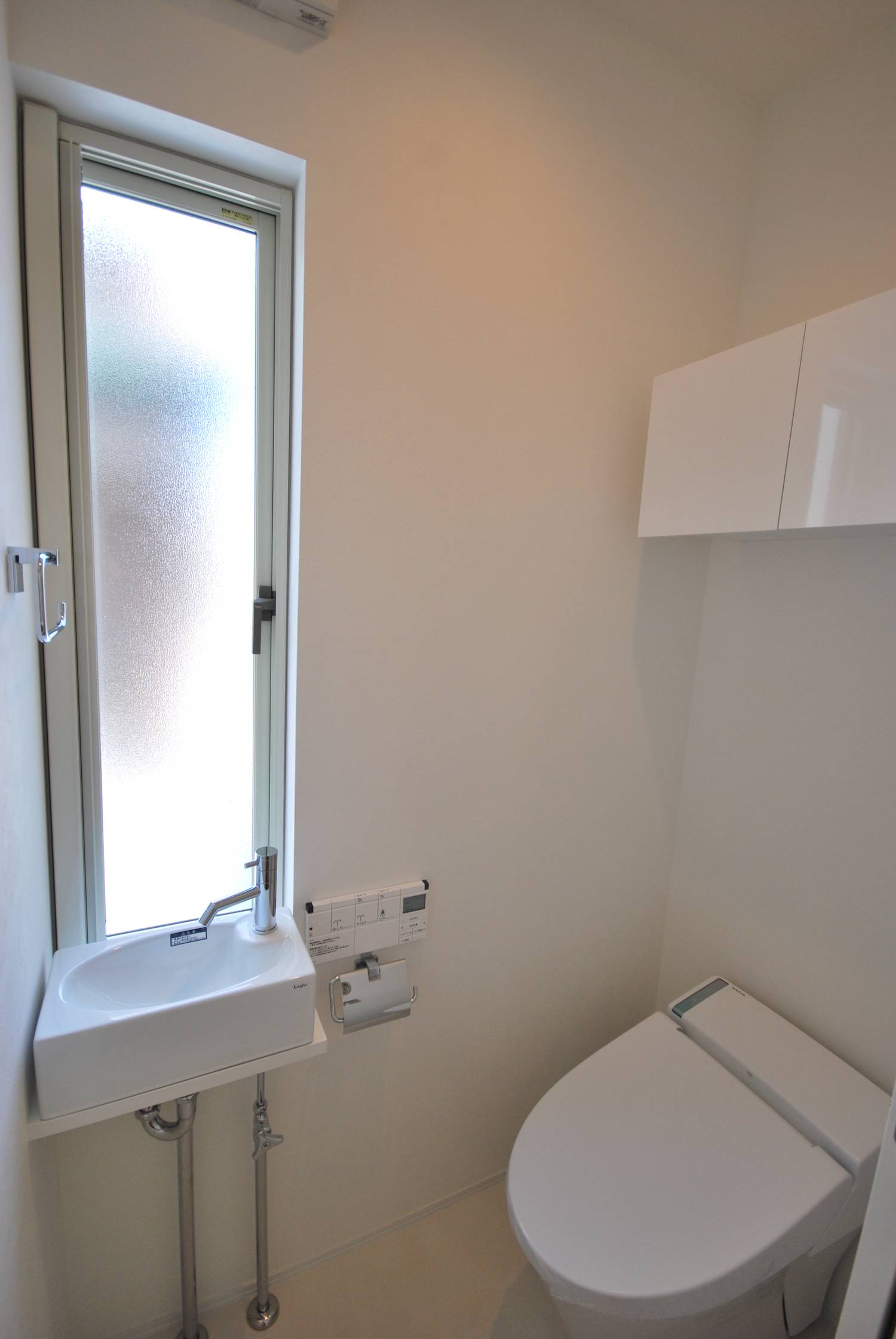 縦長のスリット窓や手洗いカウンターが取り付けられたシンプルなトイレ・デザイン住宅