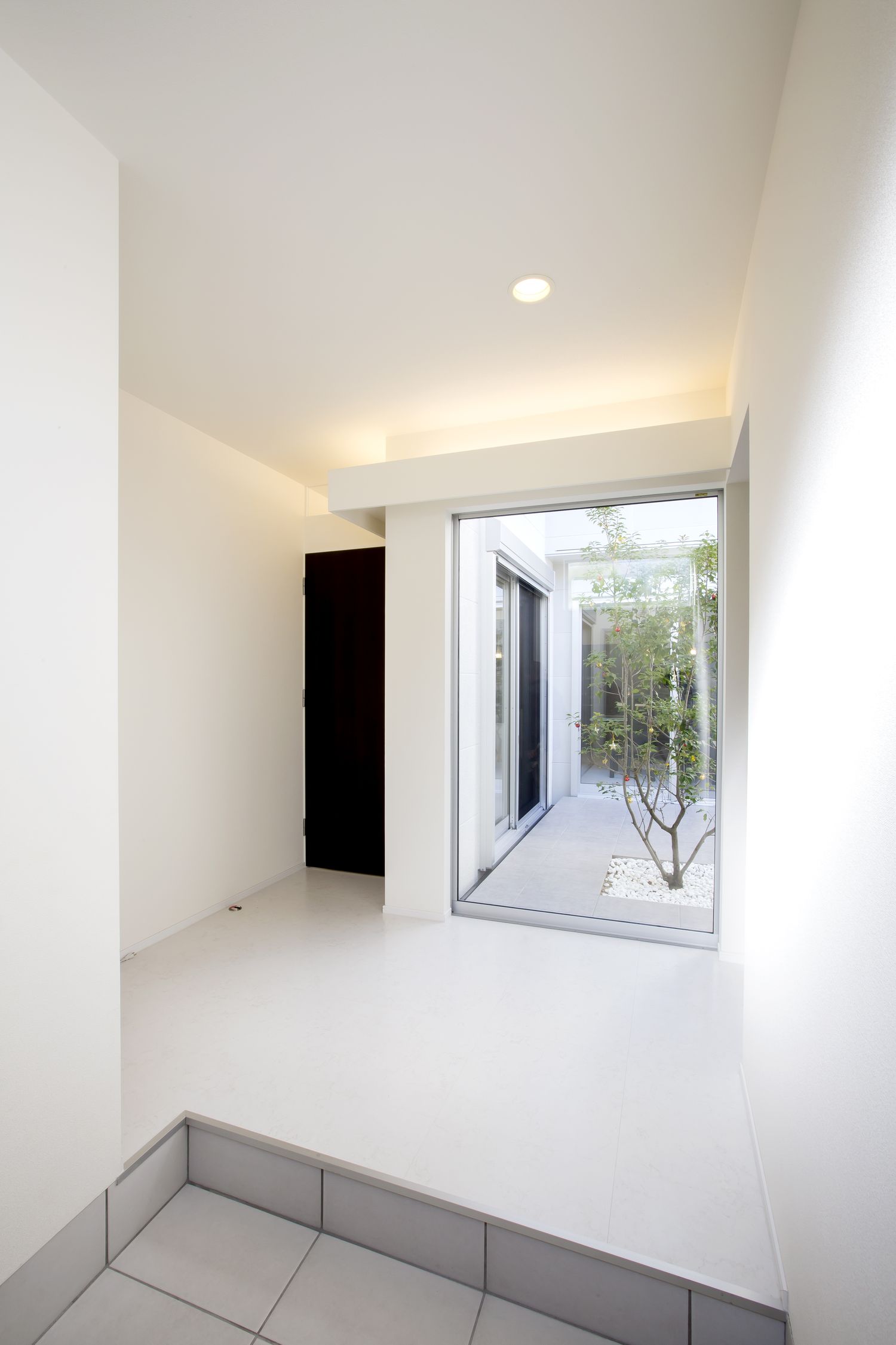 正面に中庭が見える大きな窓がある、シンプルで開放的な玄関・デザイン住宅
