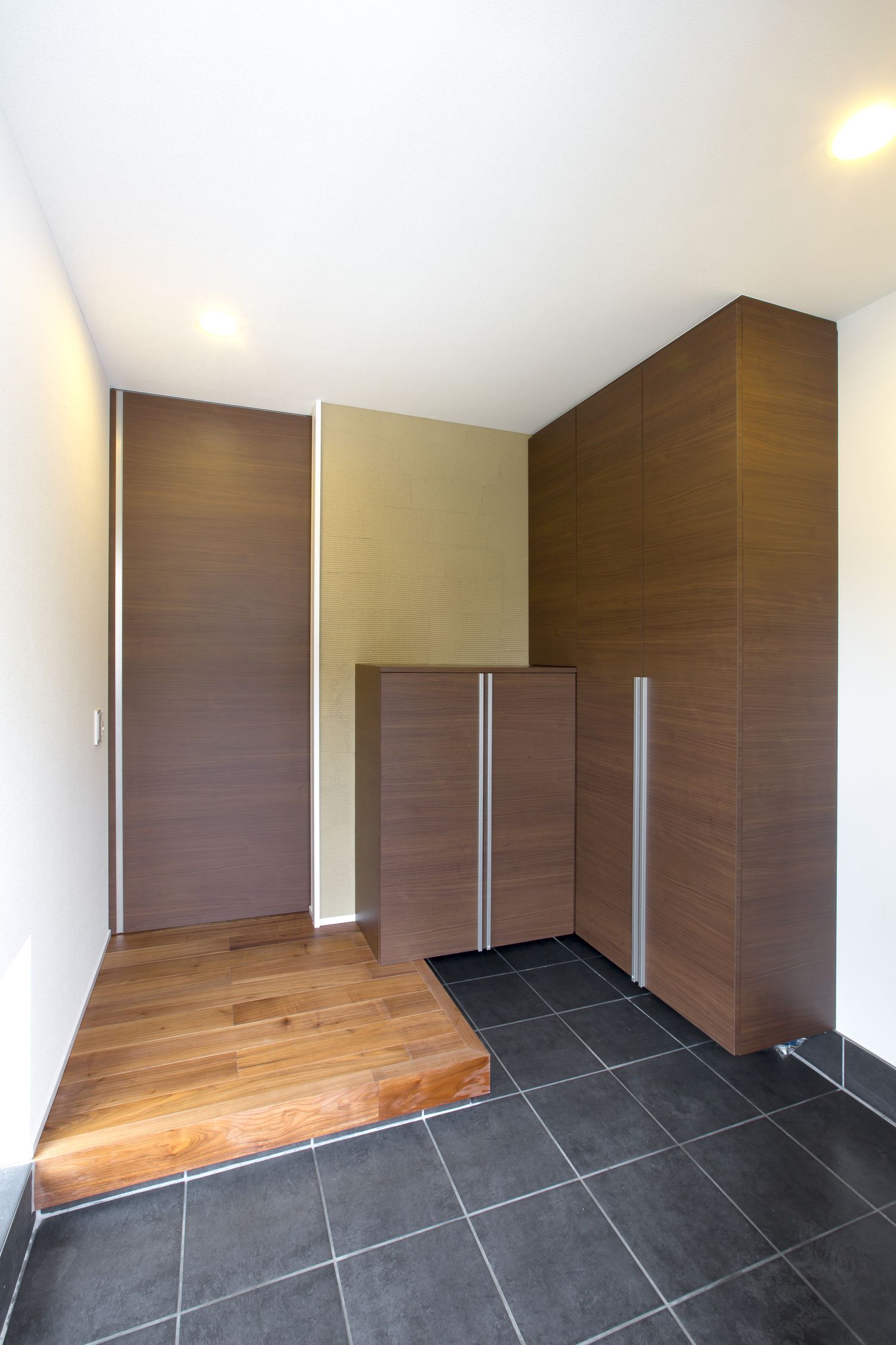 木目のシューズボックスを取り付けたシンプルなタイルの玄関・デザイン住宅