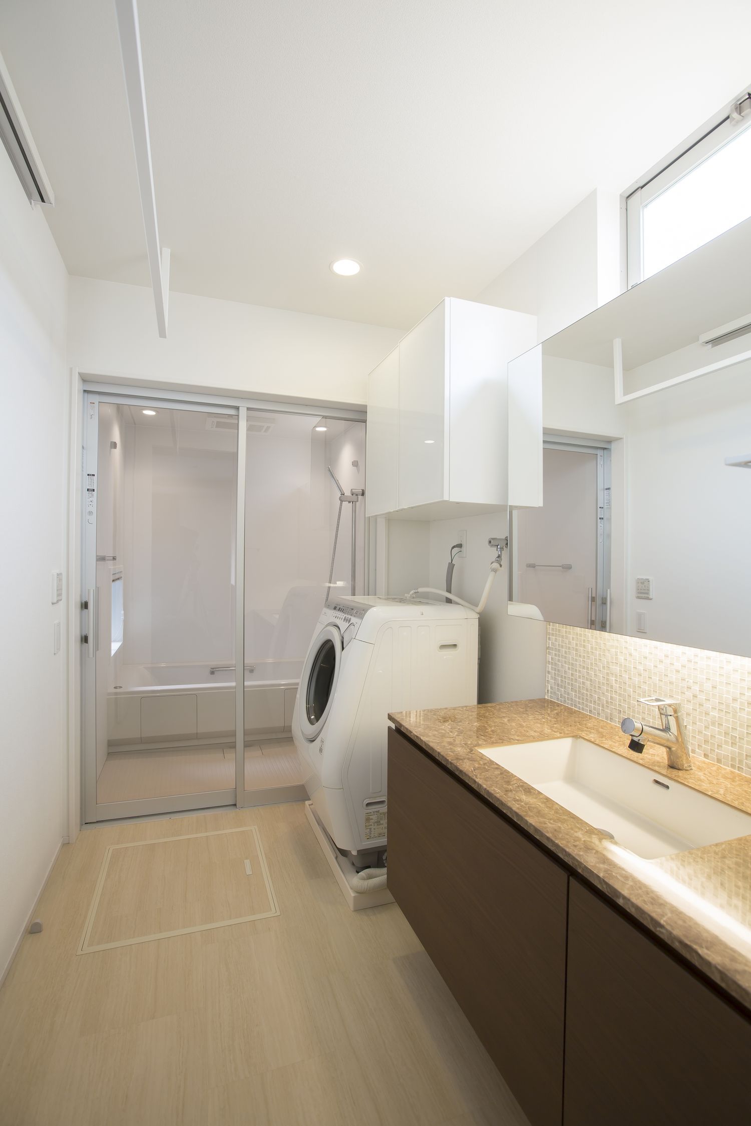 ガラス扉を取り付けた浴室があるシンプルで清潔感のある洗面所・デザイン住宅