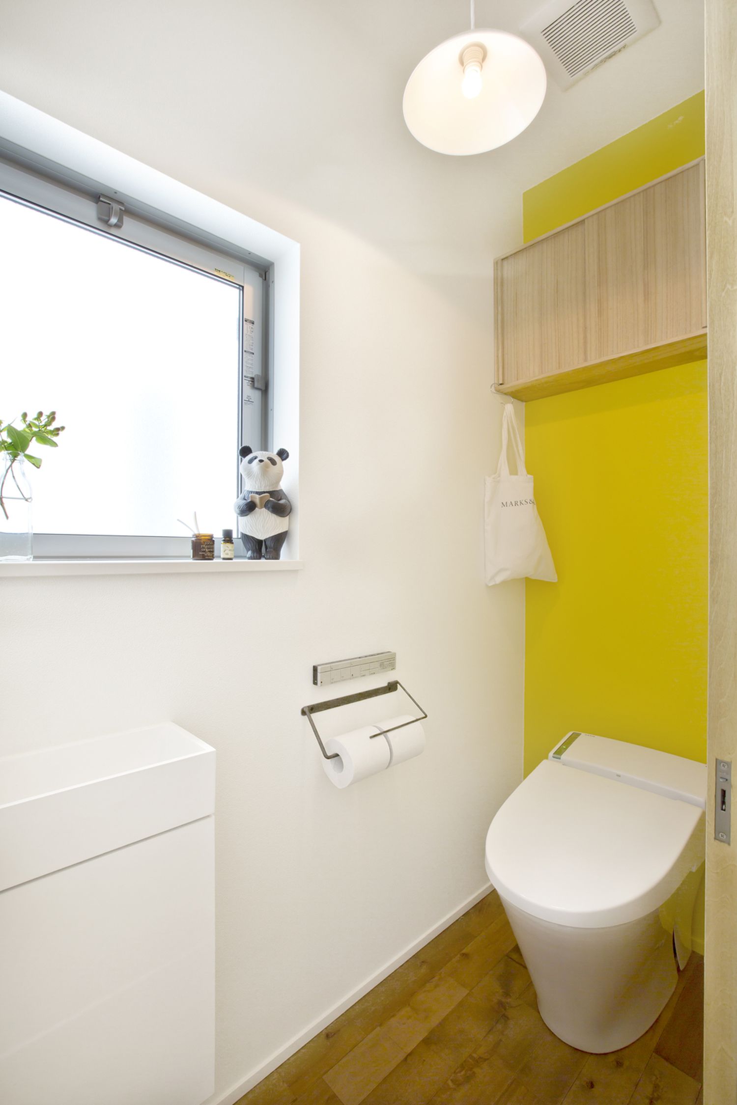 黄色のアクセントクロスに木の収納を取り付けたおしゃれなトイレ・デザイン住宅