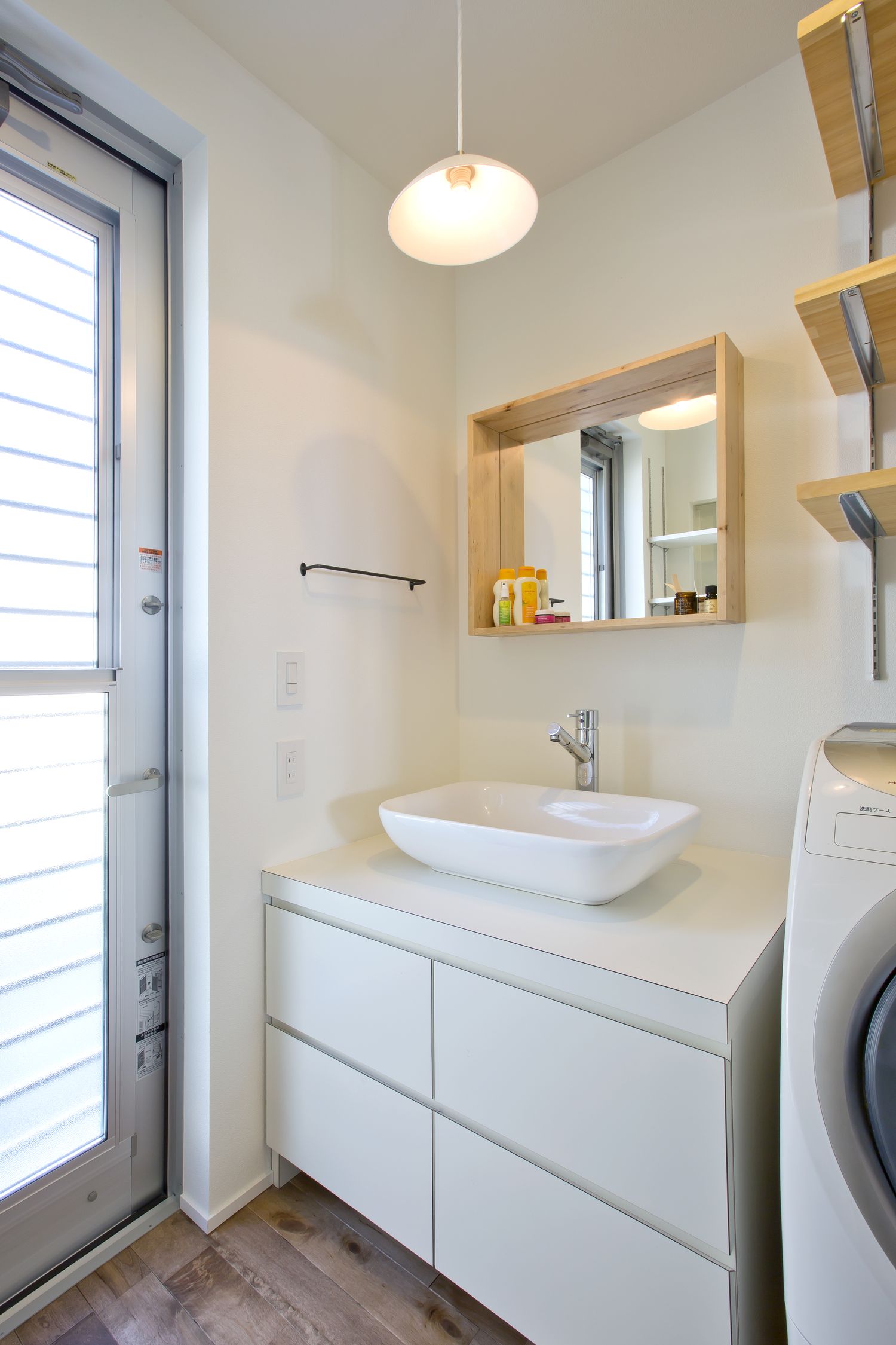 ペンダントライトや木枠の鏡を取り付けたシンプルでナチュラルな洗面所・デザイン住宅