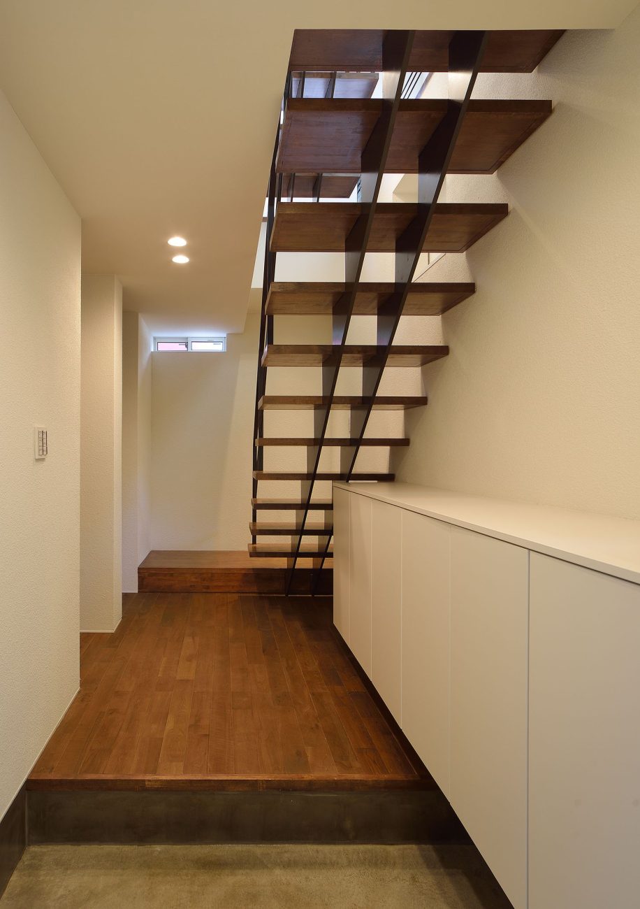 正面にスケルトン階段がある、白いシューズボックスを取り付けたシンプルな玄関・デザイン住宅