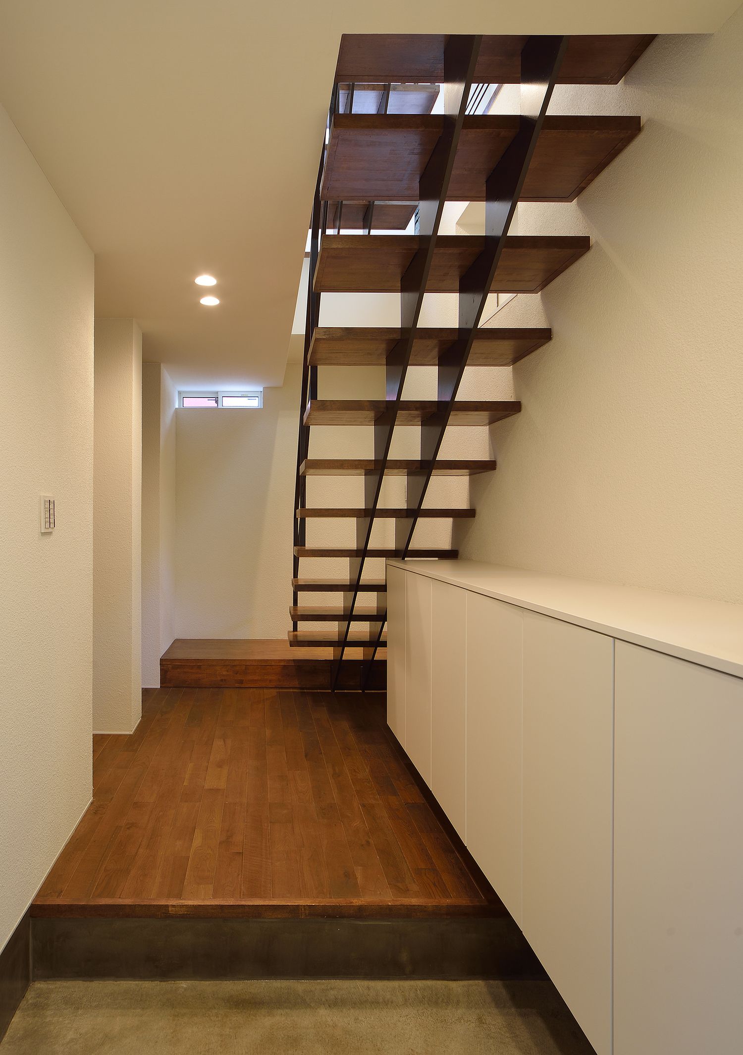 正面にスケルトン階段がある、白いシューズボックスを取り付けたシンプルな玄関・デザイン住宅