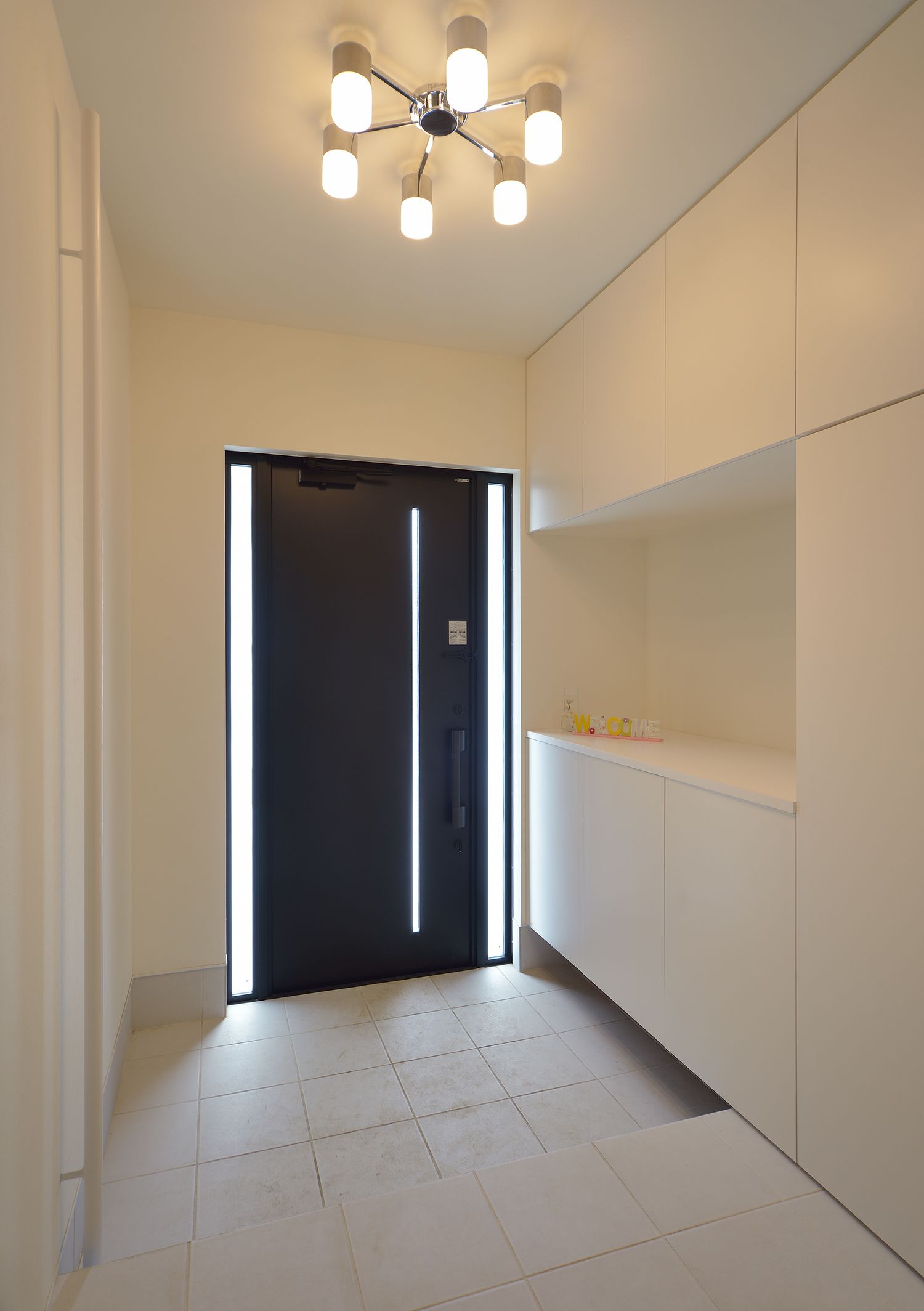 おしゃれな間接照明が取り付けられた白いタイルの玄関・デザイン住宅