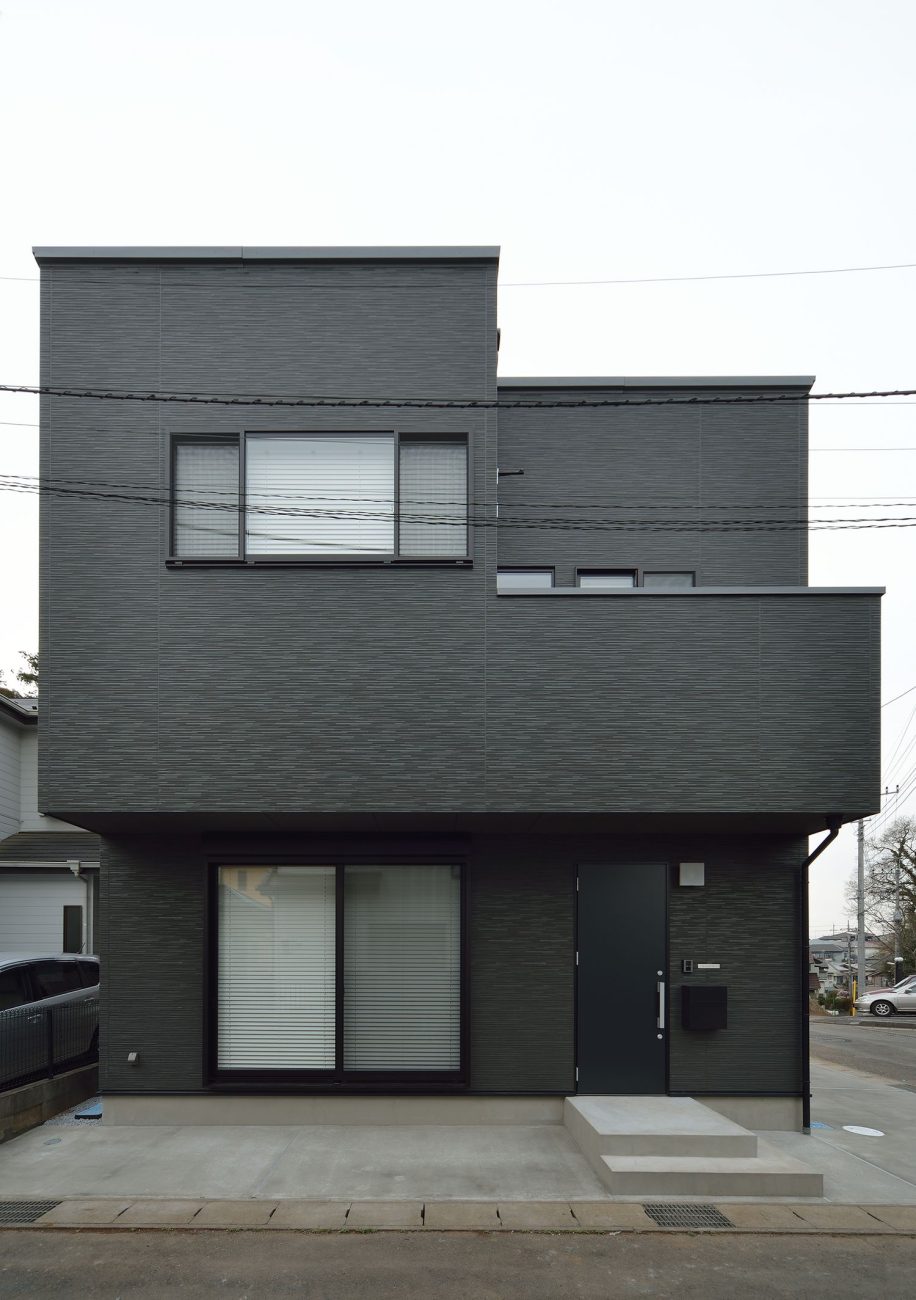 コンクリートの駐車スペースがある黒いキューブ状の外観の家・デザイン住宅