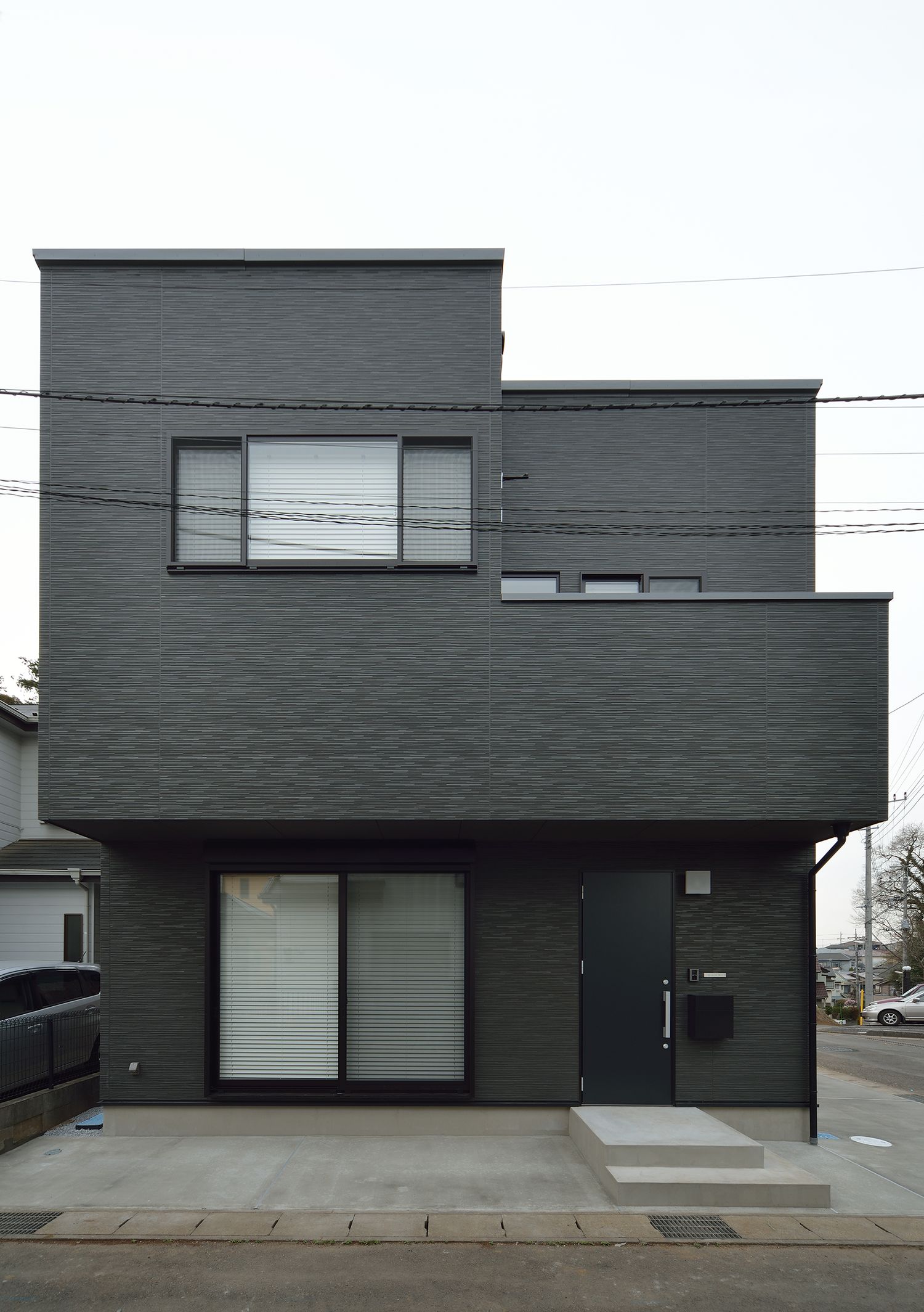 コンクリートの駐車スペースがある黒いキューブ状の外観の家・デザイン住宅