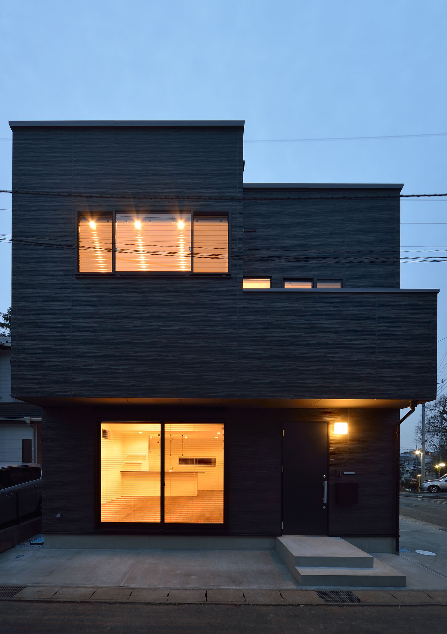 窓から光が漏れるスタイリッシュな黒い外壁の家・デザイン住宅