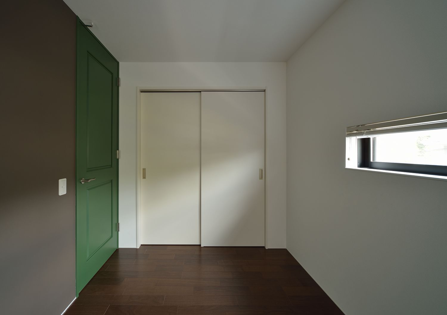 緑色の扉やスリット窓が取り付けられたコンパクトな寝室・デザイン住宅