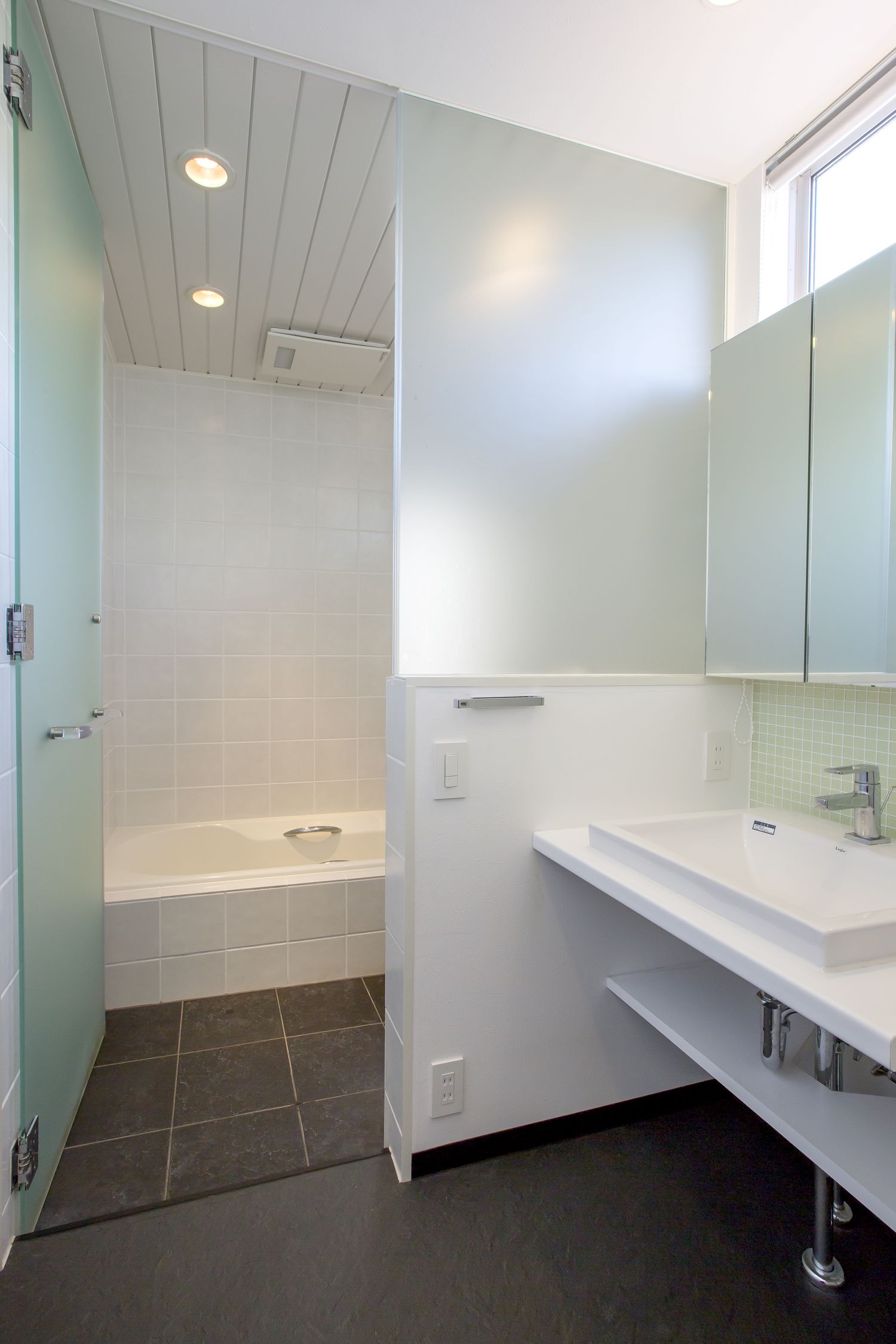 すりガラスの扉を取り付けた浴室の隣にある、シンプルな洗面所・デザイン住宅