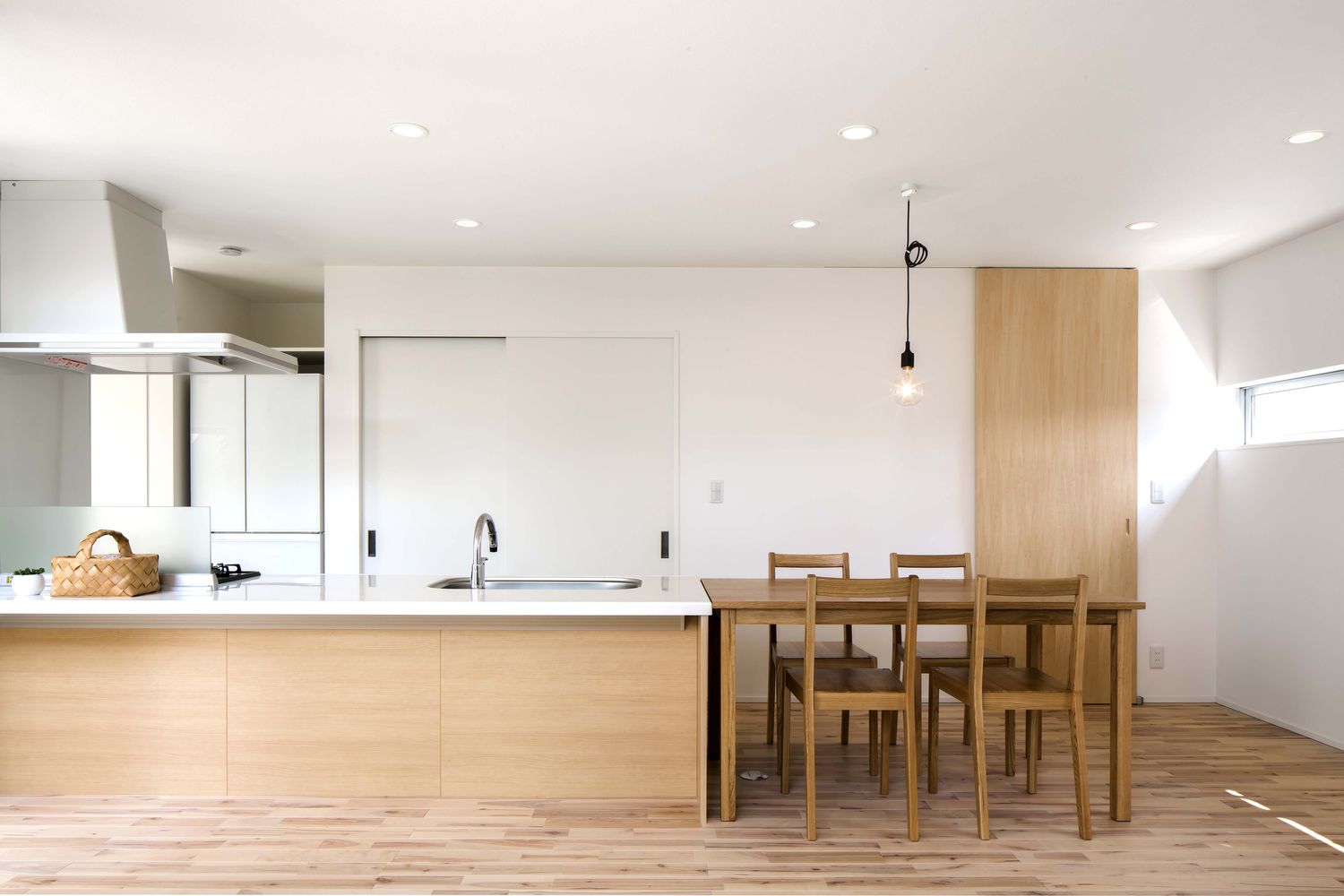 キッチンと横並びになった木のダイニングテーブルがあるすっきりとしたLDK・デザイン住宅