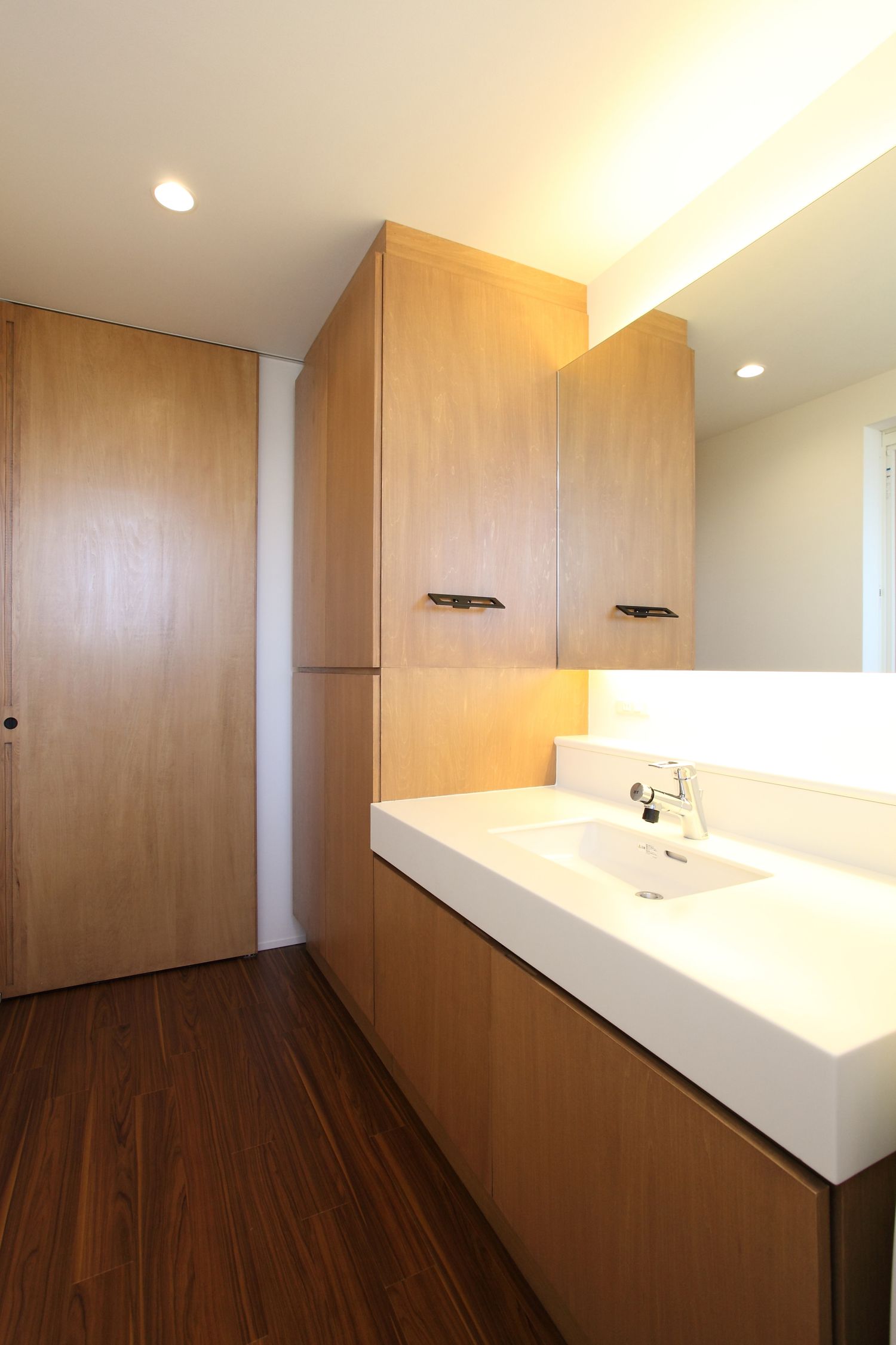 鏡の裏に間接照明がある木の収納棚を取り付けた洗面所・デザイン住宅