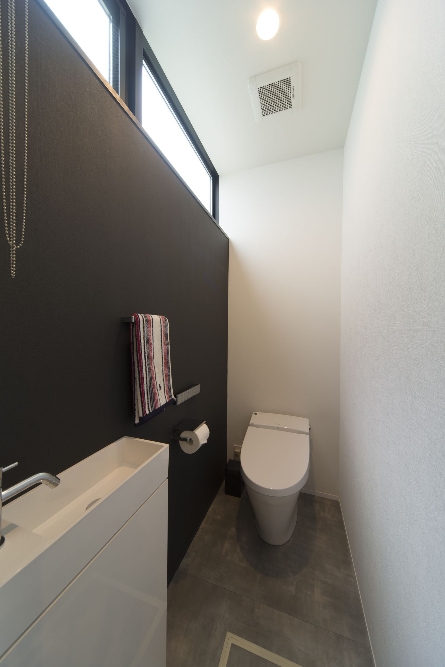 黒いアクセントクロスに薄型手洗いを取り付けたトイレ・デザイン住宅