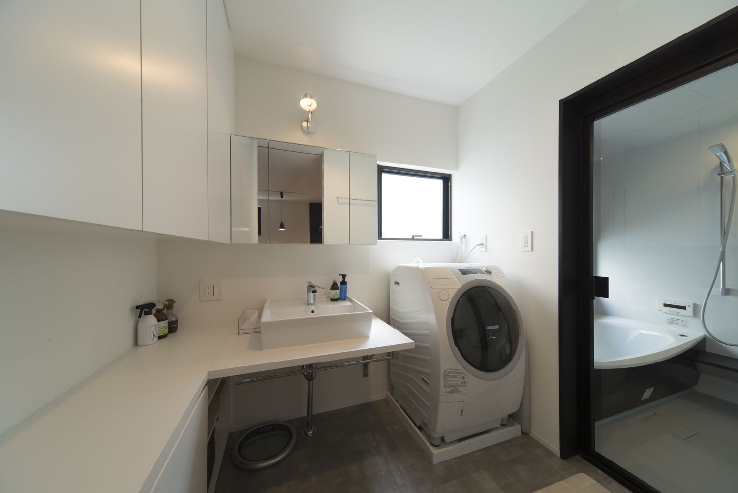 ガラス扉付きの浴室と隣合ったモノトーンのシンプルな洗面所・デザイン