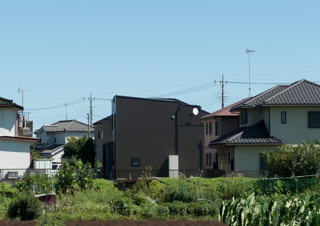 畑越しに窓の無い黒い外壁の住宅が見える様子・デザイン住宅 注文住宅・デザイン住宅建築実例_『CASE638 「BLACK BOX」』_外観