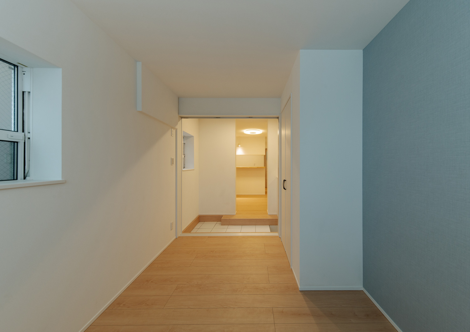 水色のアクセントクロスを設けたフローリングの個室から玄関が見える様子・デザイン住宅 注文住宅・デザイン住宅建築実例_『CASE641 だんだん』_寝室