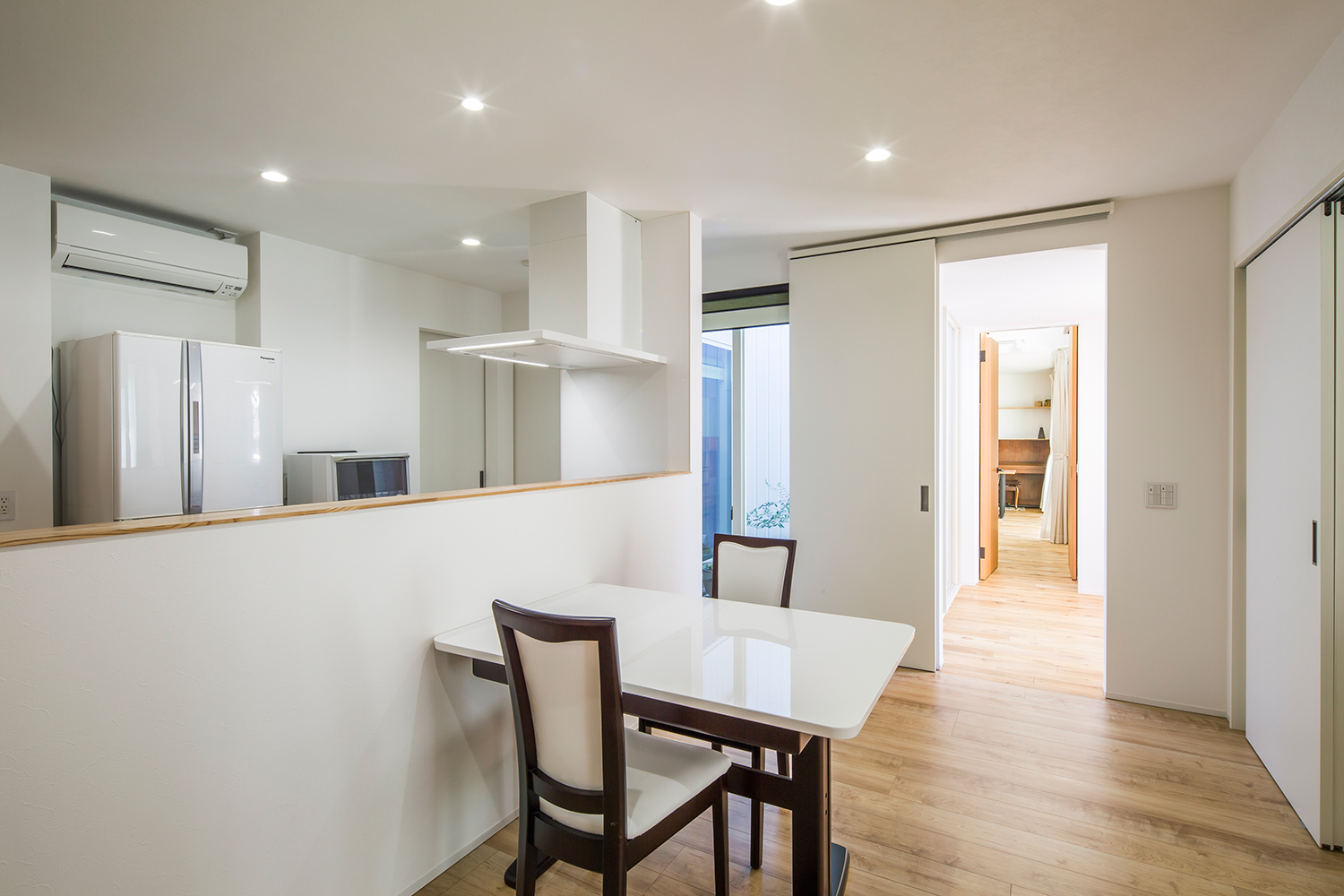 腰壁付きのカウンターキッチンの前に、二人掛けの白いダイニングテーブルを置いたLDK・デザイン住宅 注文住宅・デザイン住宅建築実例_『CASE635 三角屋根でつながる家』_LDK