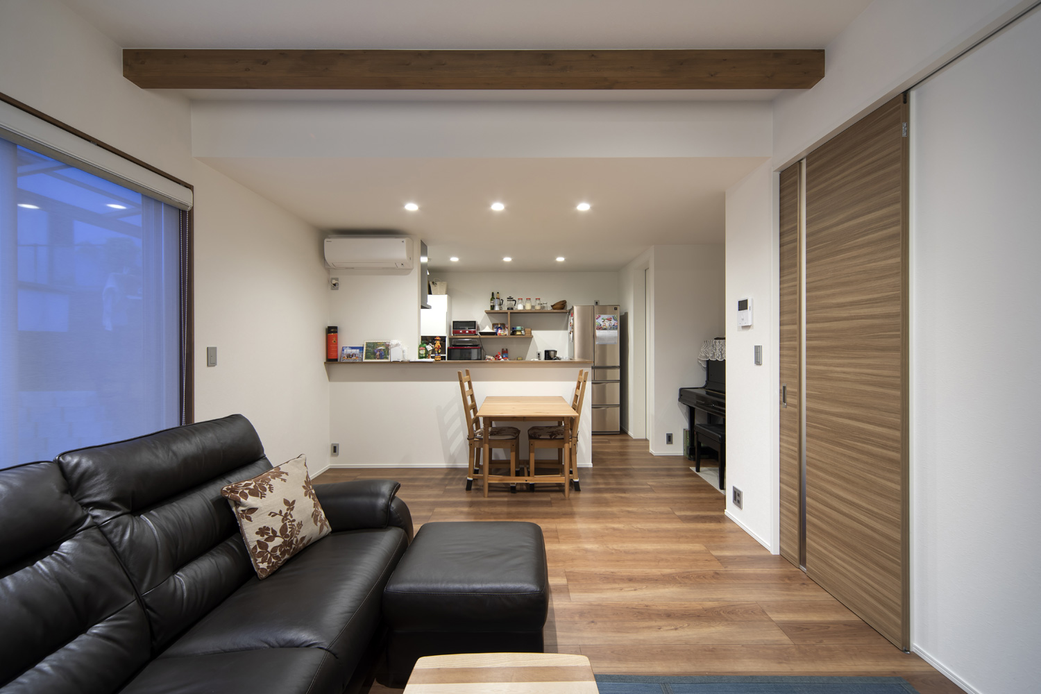 リビングから木のダイニングテーブルや腰壁付きのペニンシュラキッチンを見た様子・デザイン住宅 注文住宅・デザイン住宅建築実例_『CASE644 Oasis』_LDK