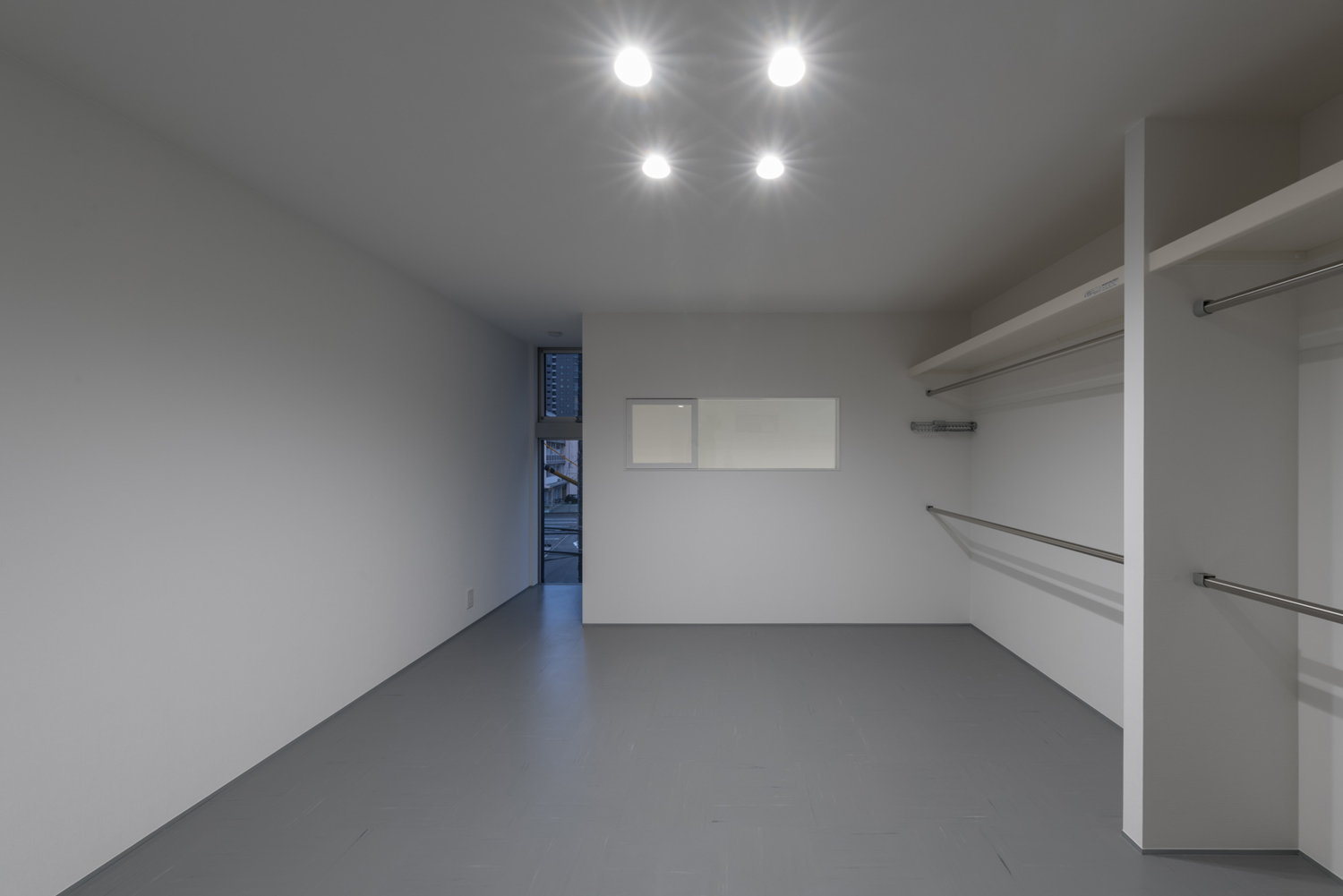 壁一面にハンガーラックがあり、縦長のスリット窓が取り付けられたグレーの床の空間・デザイン住宅 注文住宅・デザイン住宅建築実例_『CASE646 鏡の家』_寝室