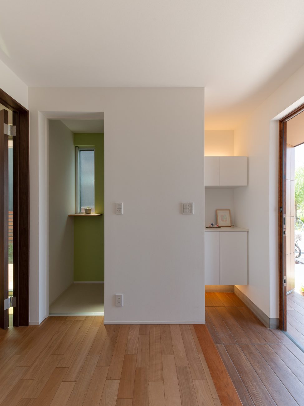 白い壁の間から黄緑のクロスが見えるフローリングの廊下・デザイン住宅 注文住宅・デザイン住宅建築実例_『CASE647 ニコニコハウス』_玄関