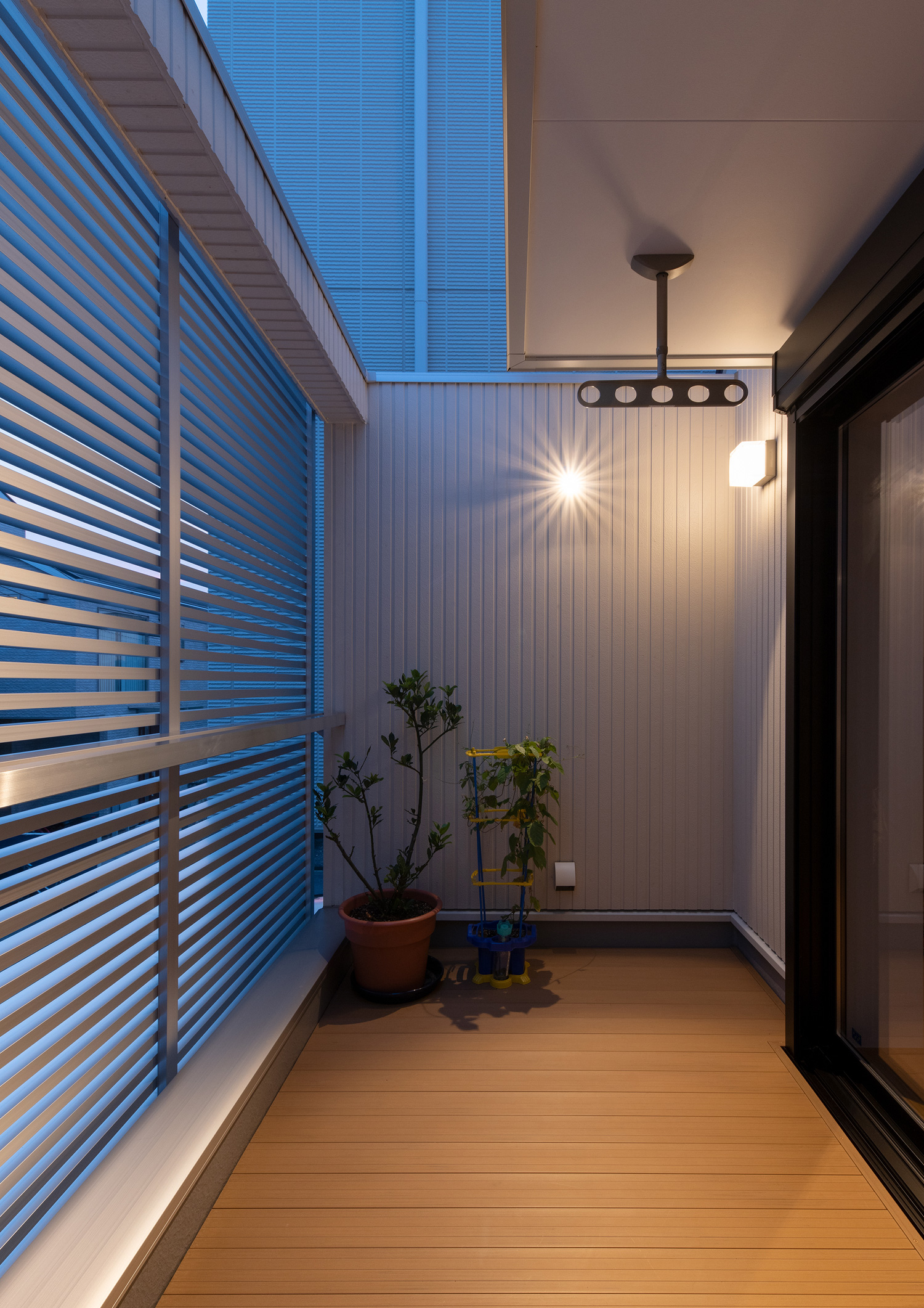 アルミのルーバーで目隠しがされたウッドデッキのバルコニーの壁に、照明が取り付けられた様子・デザイン住宅 注文住宅・デザイン住宅建築実例_『CASE648 白鍵の家』_テラス・バルコニー