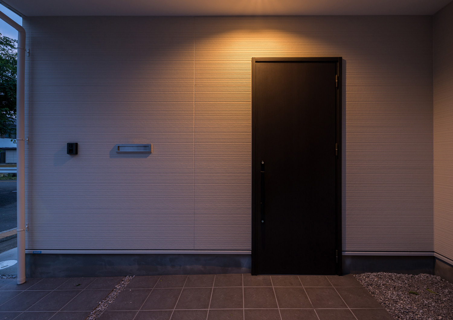 白い外壁にダークブラウンの玄関扉が設けられ、壁が照明によって照らされている様子・デザイン住宅 注文住宅・デザイン住宅建築実例_『CASE650 景色を持つ家』_外観