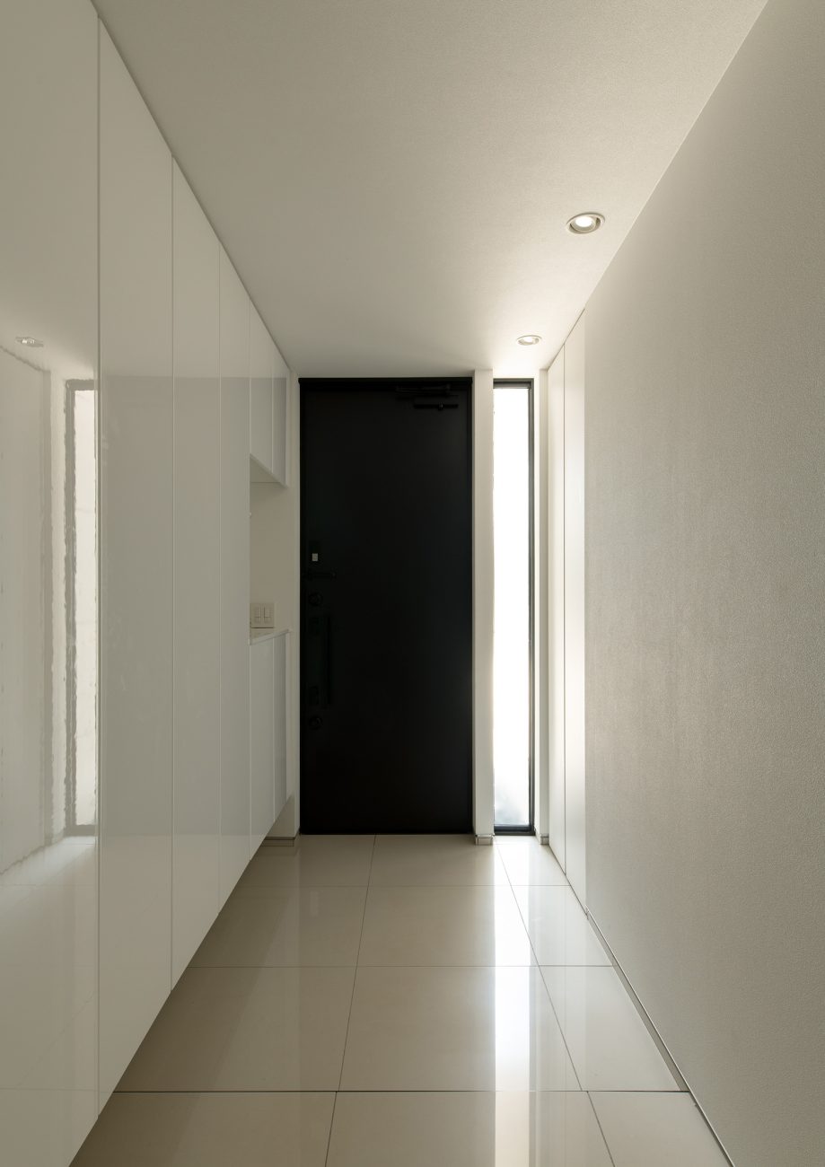 黒い玄関扉の横に縦長のスリット窓が設けられた白いタイルの玄関・デザイン住宅 注文住宅・デザイン住宅建築実例_『CASE653 せんのいえ』_玄関