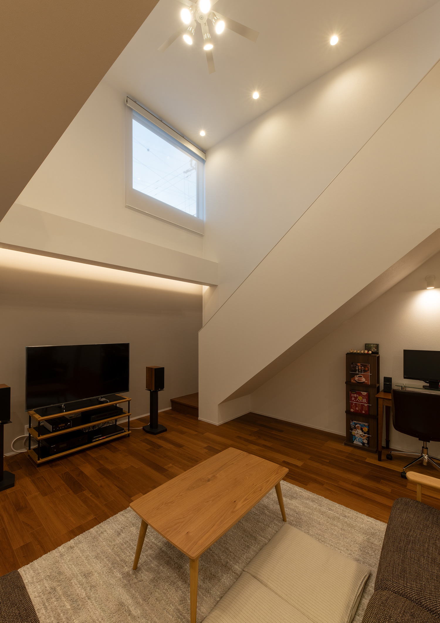 シーリングファンに照明が取り付けられ、テレビの上に間接照明が取り付けられた吹き抜けのLDK・デザイン住宅 注文住宅・デザイン住宅建築実例_『CASE658 connecting terminal』_LDK