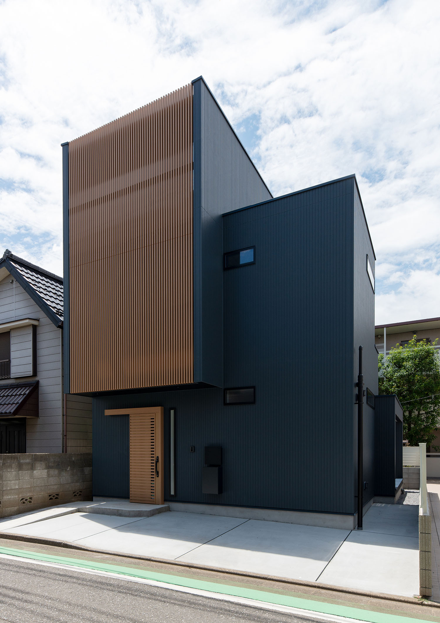紺色の外壁にルーバーの目隠しや木の玄関扉がついた住宅を斜めから見た様子・デザイン住宅 注文住宅・デザイン住宅建築実例_『CASE660 Marine et grille』_外観