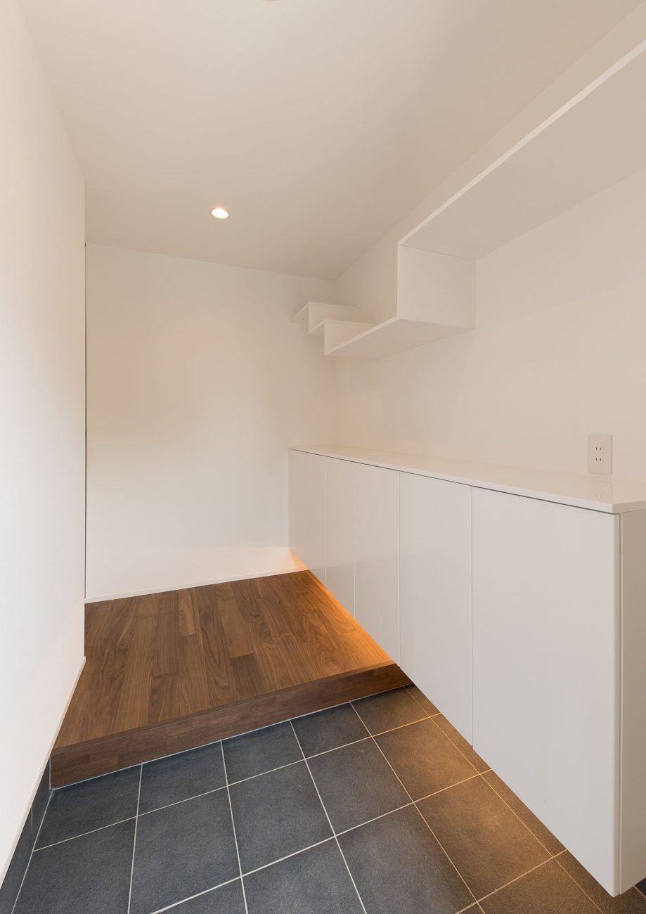 白い浮き収納の下に間接照明が取り付けられたグレーのタイルの玄関・デザイン住宅 注文住宅・デザイン住宅建築実例_『CASE662 まくのいえ』_玄関