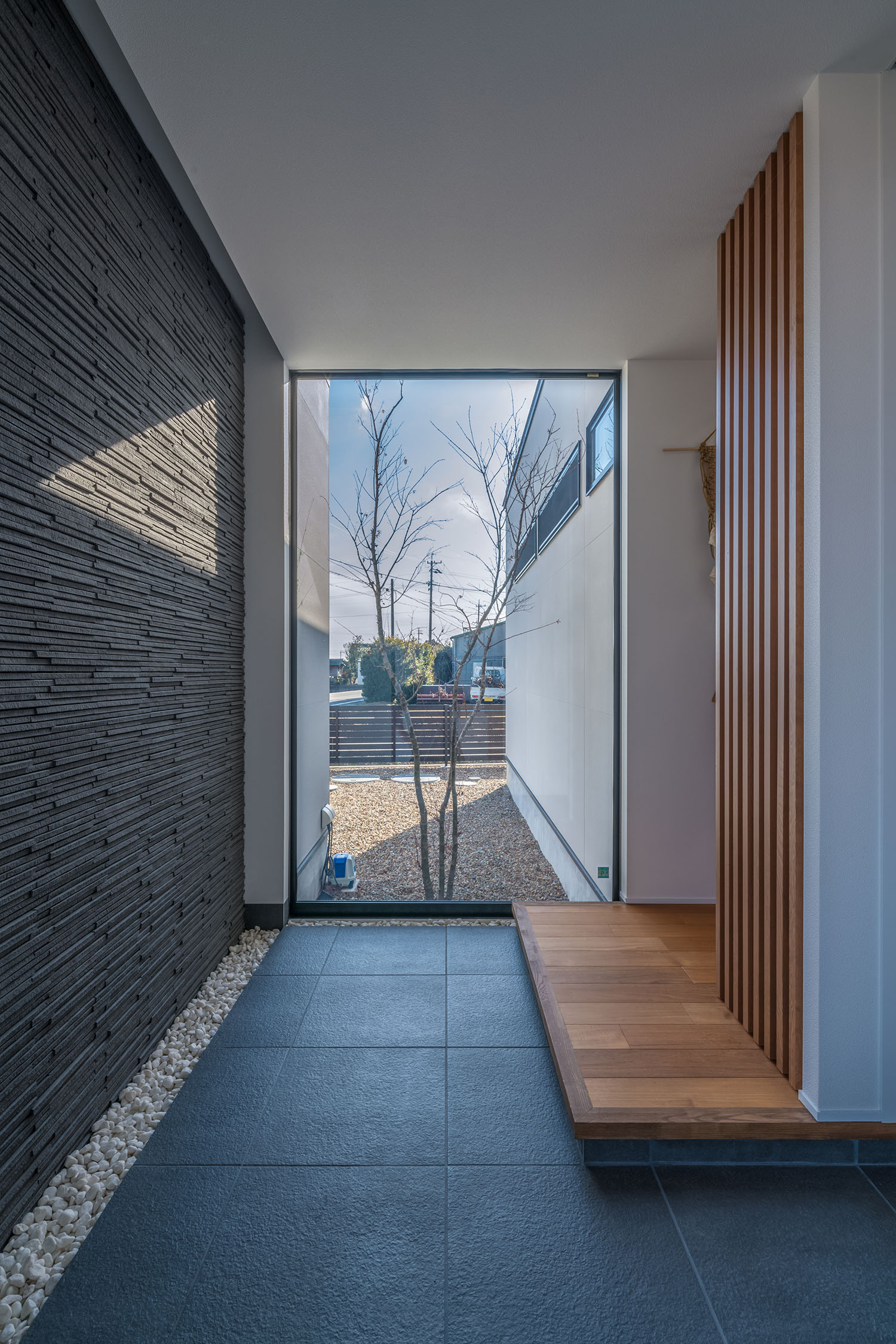 タイルの玄関の正面がFIX窓になっており、そこからシンボルツリーが見える様子・デザイン住宅 注文住宅・デザイン住宅建築実例_『CASE671 実りの平屋』_玄関