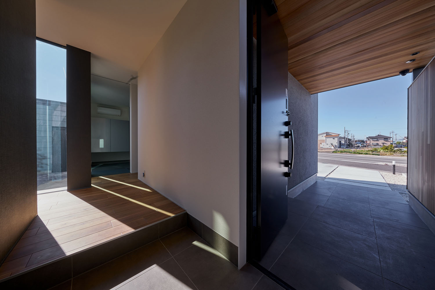木目の軒天井になっている玄関ポーチから玄関の内部まで黒いタイルが繋がっている様子・デザイン住宅 注文住宅・デザイン住宅建築実例_『CASE670 静かな形の家』_玄関