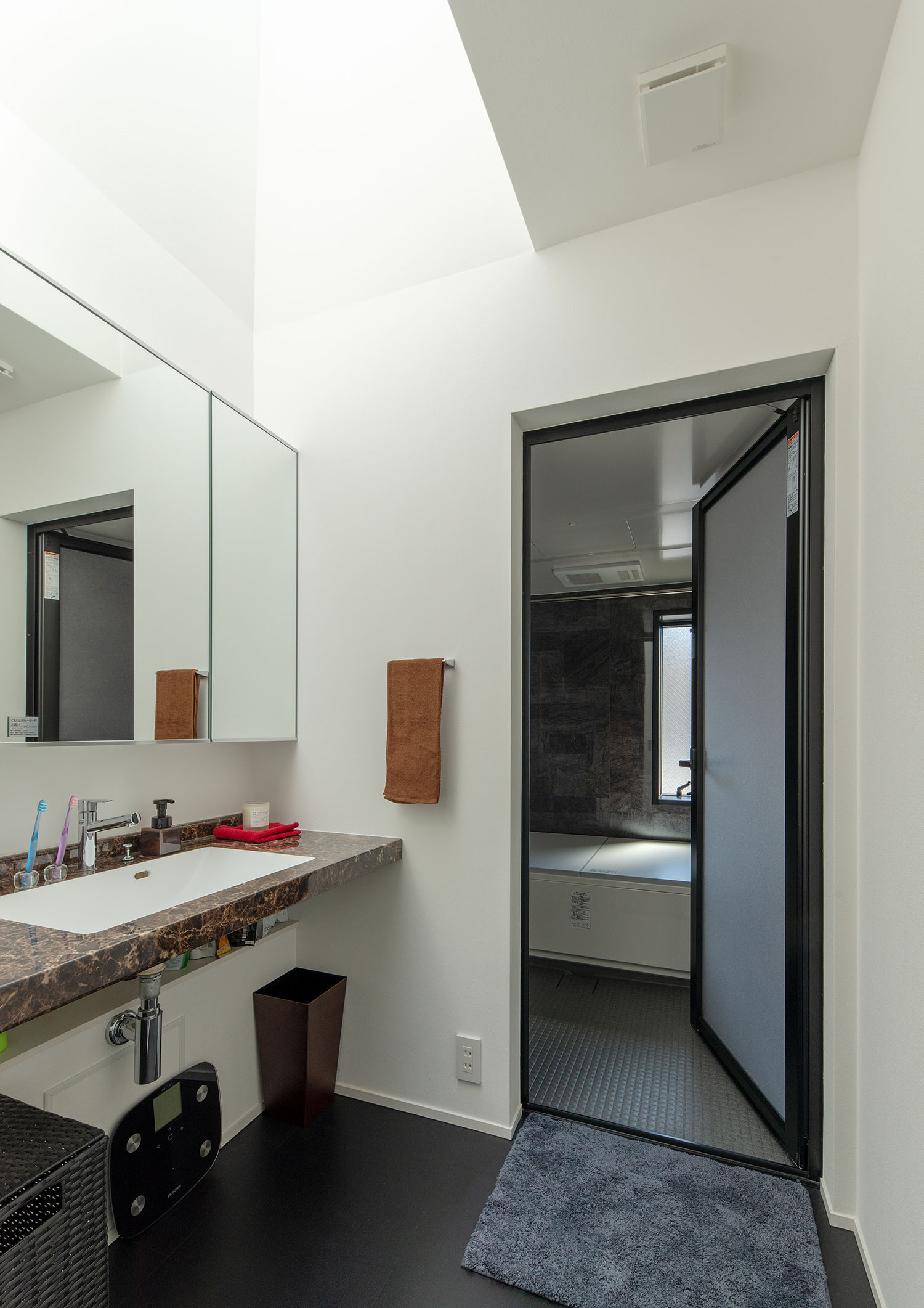 トップライトを取り付けた洗面所から、黒い壁の浴室へと繋がる様子・ラグジュアリーな住宅 注文住宅・デザイン住宅建築実例_『CASE673 Ganache』_浴室・洗面所