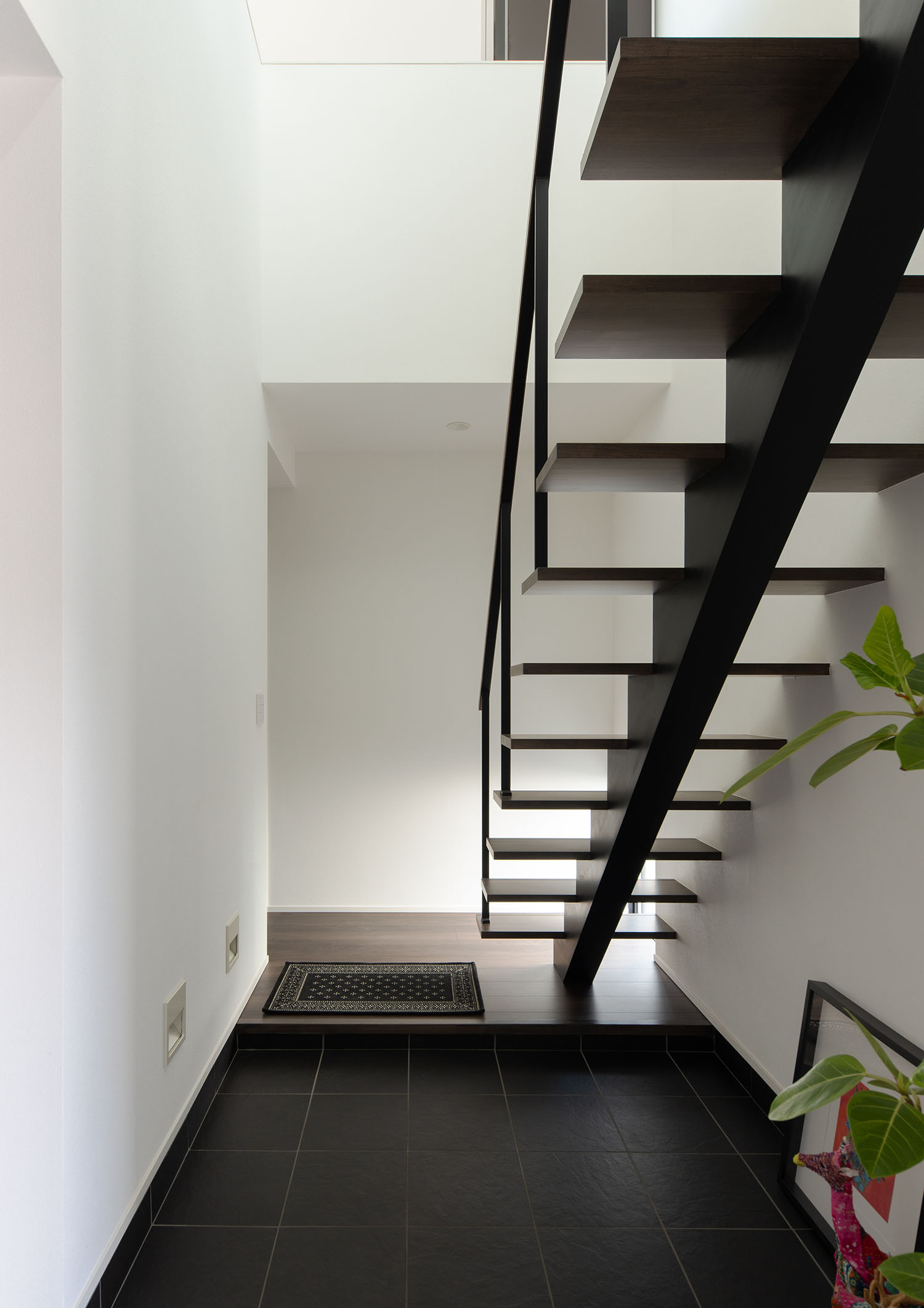 黒いタイルの玄関のそばにあるスケルトン階段・ラグジュアリーな住宅 注文住宅・デザイン住宅建築実例_『CASE673 Ganache』_玄関