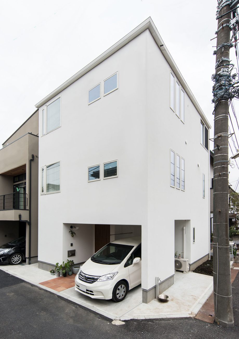 角地に建つ、白いキューブ状の三階建て住宅に白い車が一台止められている様子・デザイン住宅 注文住宅・デザイン住宅建築実例_『CASE674 Gardenのある家』_外観