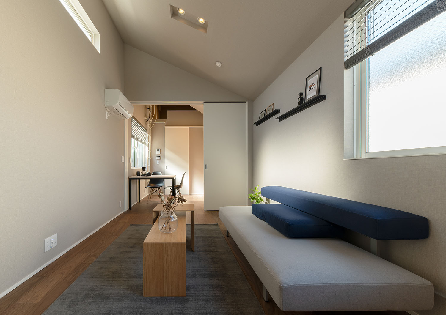 青いソファーと、観葉植物の乗ったテーブルがあるリビングからダイニングを見た様子・賃貸併用住宅 注文住宅・デザイン住宅建築実例_『CASE681  penche'　「パンシェ」の家』_LDK