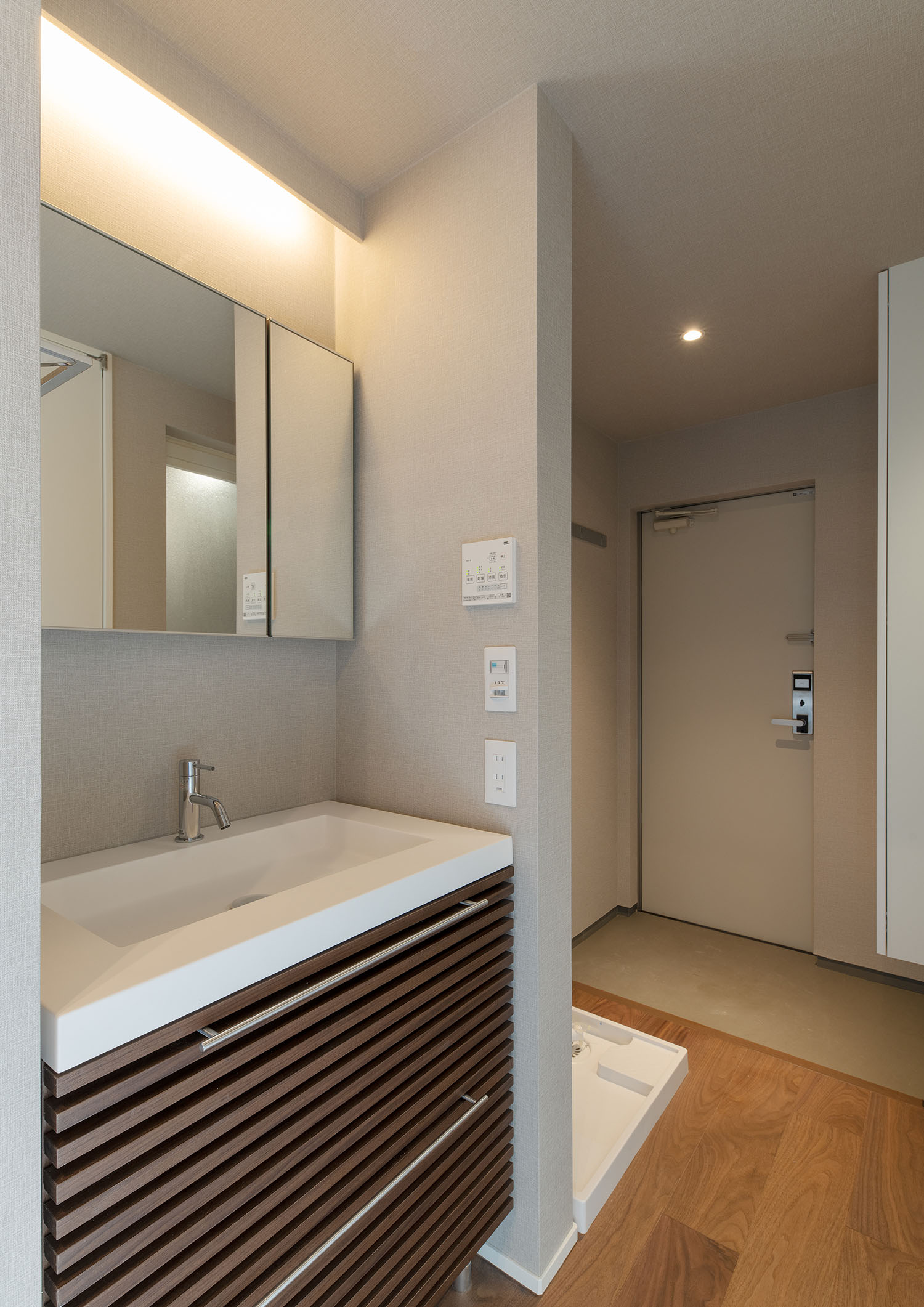 木の引き出しや間接照明が設けられた洗面所越しに玄関が見える様子・賃貸併用住宅 注文住宅・デザイン住宅建築実例_『CASE681  penche'　「パンシェ」の家』_浴室・洗面所