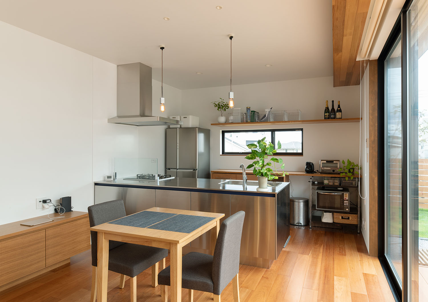 ステンレスのペニンシュラキッチンの前に、二人掛けのダイニングテーブルが置かれている様子・デザイン住宅 注文住宅・デザイン住宅建築実例_『CASE683  丘の上のハウス』_LDK