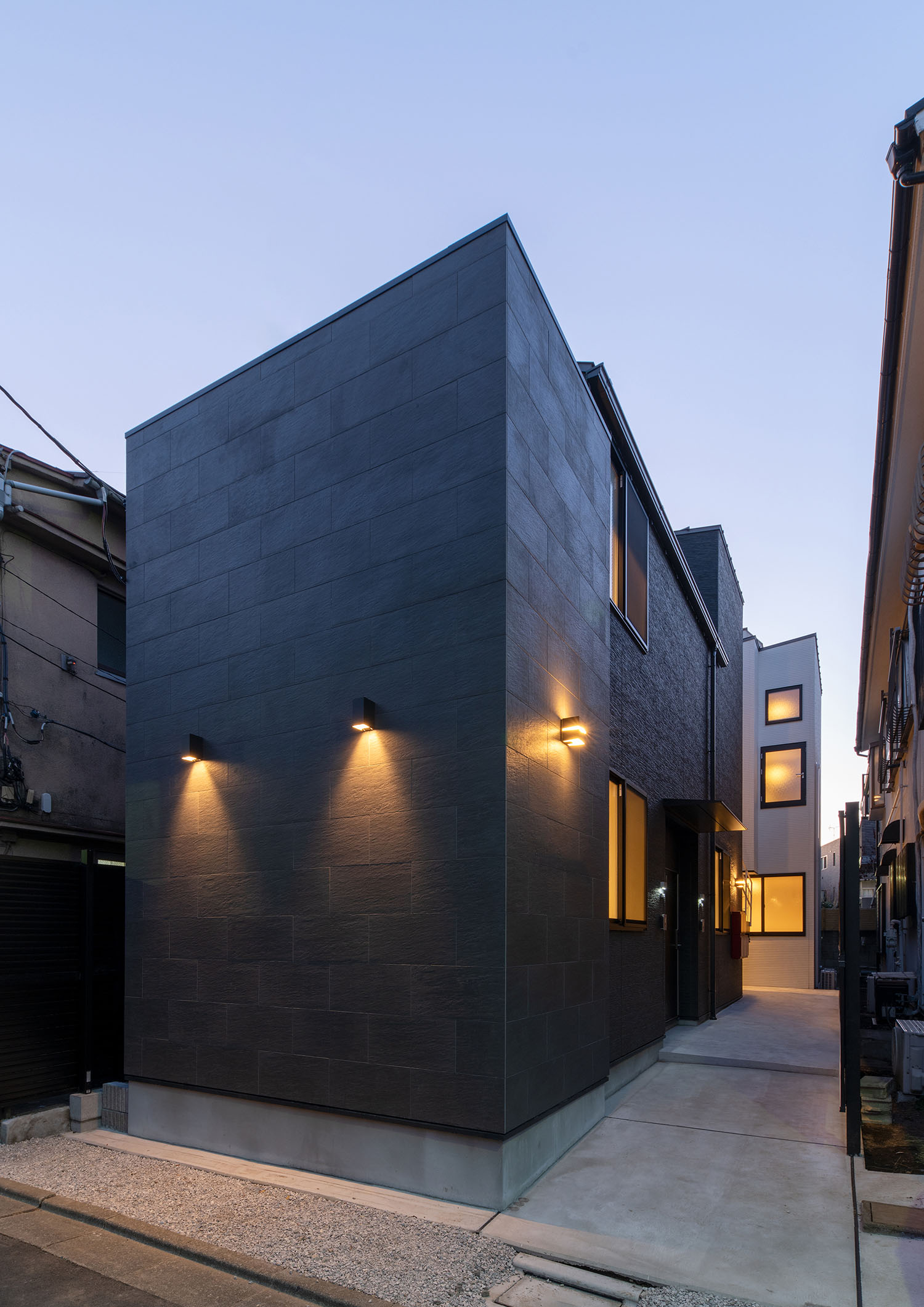 外壁に取り付けられた照明が黒い外壁の建物を照らす様子・賃貸併用住宅 注文住宅・デザイン住宅建築実例_『CASE681  penche'　「パンシェ」の家』_外観