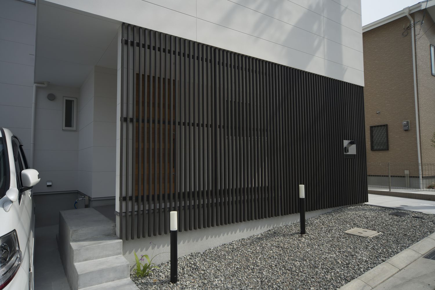 黒いルーバーの目隠しを取り付けた玄関アプローチ・デザイン住宅